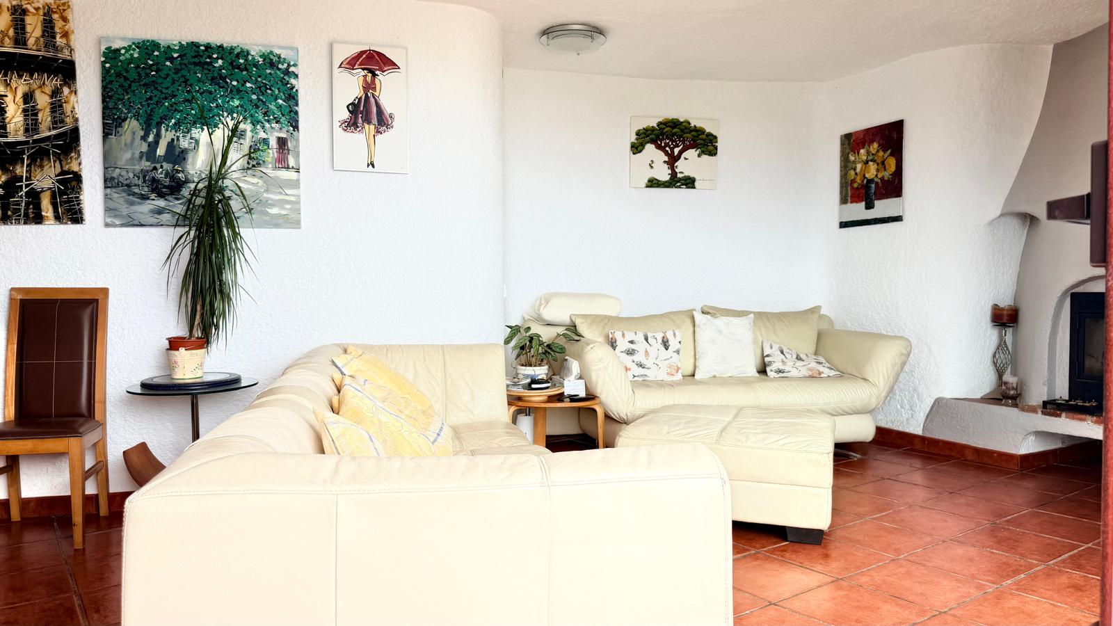 Living area featuring a wood-burning fireplace, white textured walls, terracotta flooring, and cream leather sofas arranged within a curved architectural layout.
