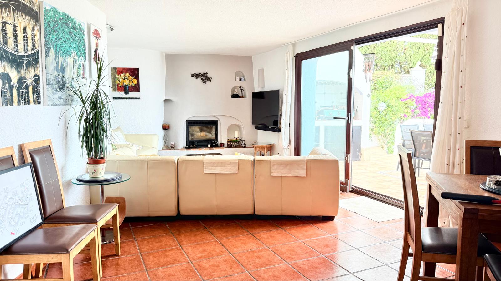 Living-dining area featuring a built-in wood fireplace, rustic tile flooring, and large sliding doors opening onto the sun-drenched Mediterranean terrace.