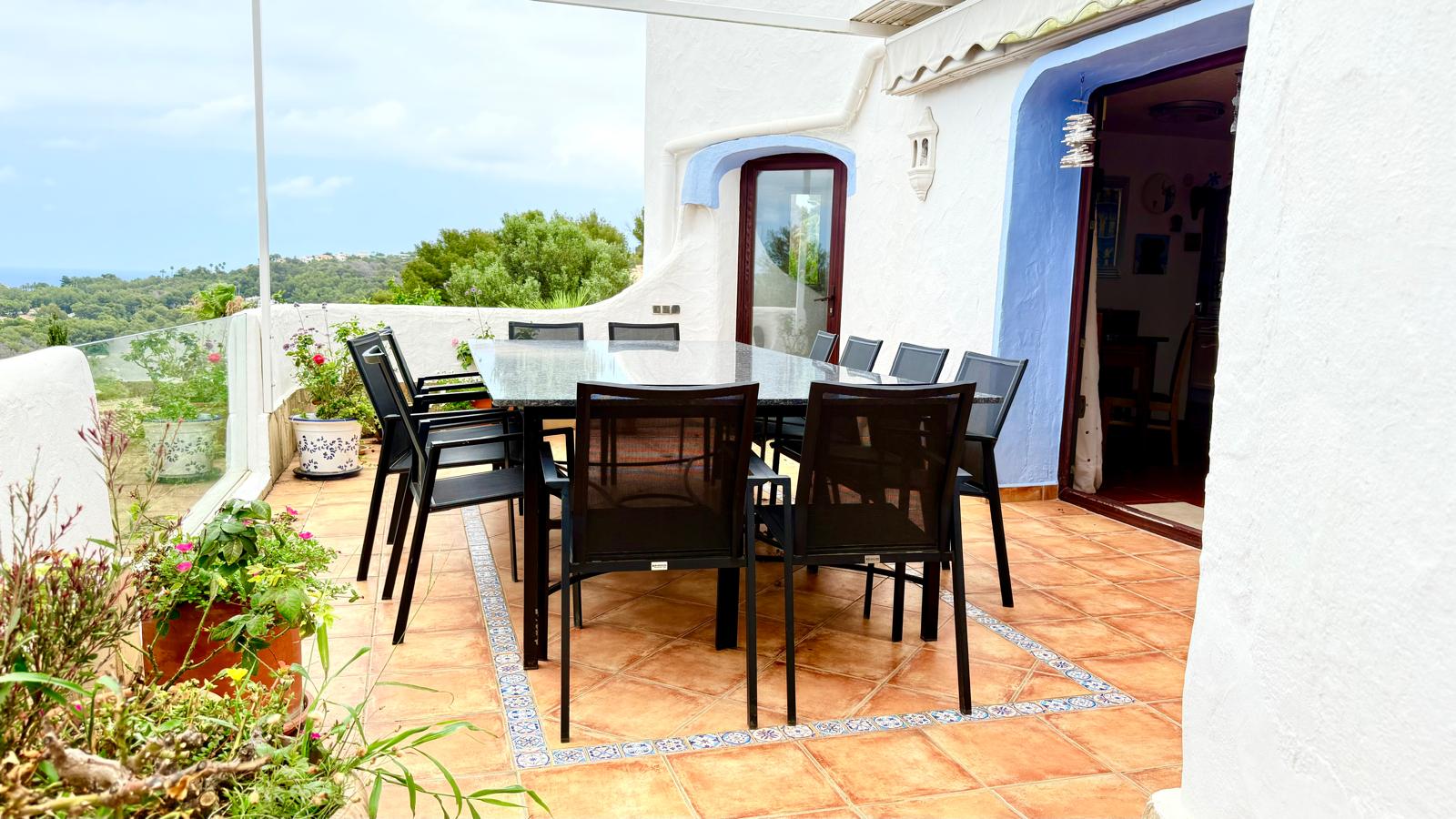 Outdoor dining terrace featuring a granite table, terracotta tiles with decorative borders, and elevated views over the Mediterranean landscape.