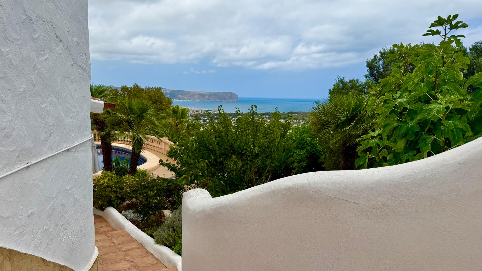 Panoramic sea views over Jávea bay from the outdoor stairs, featuring traditional white curved walls and lush Mediterranean gardens with palm trees.
