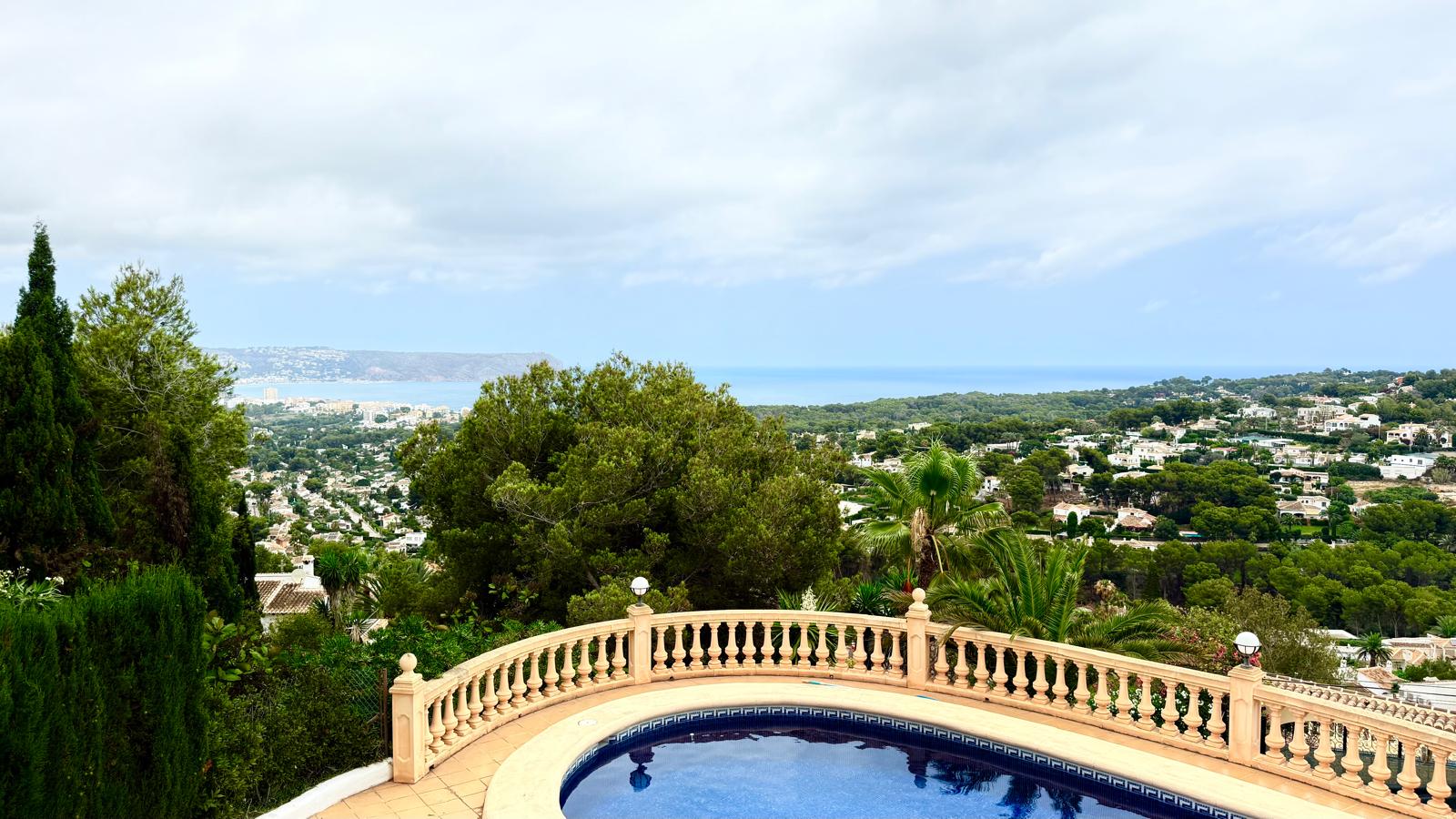 Panoramic views of the Mediterranean Sea and Jávea bay from the upper terrace, featuring a classic stone balustrade overlooking the private pool area.