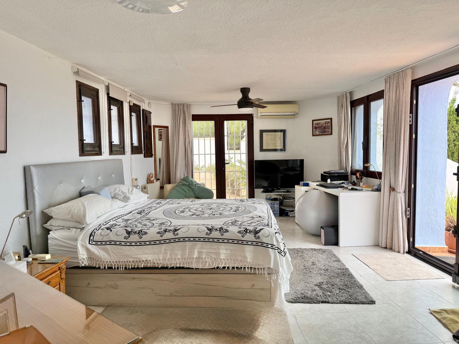 Spacious master bedroom featuring a dedicated workspace, ceiling fan, and air conditioning. Large sliding glass doors provide direct access to the private terrace.