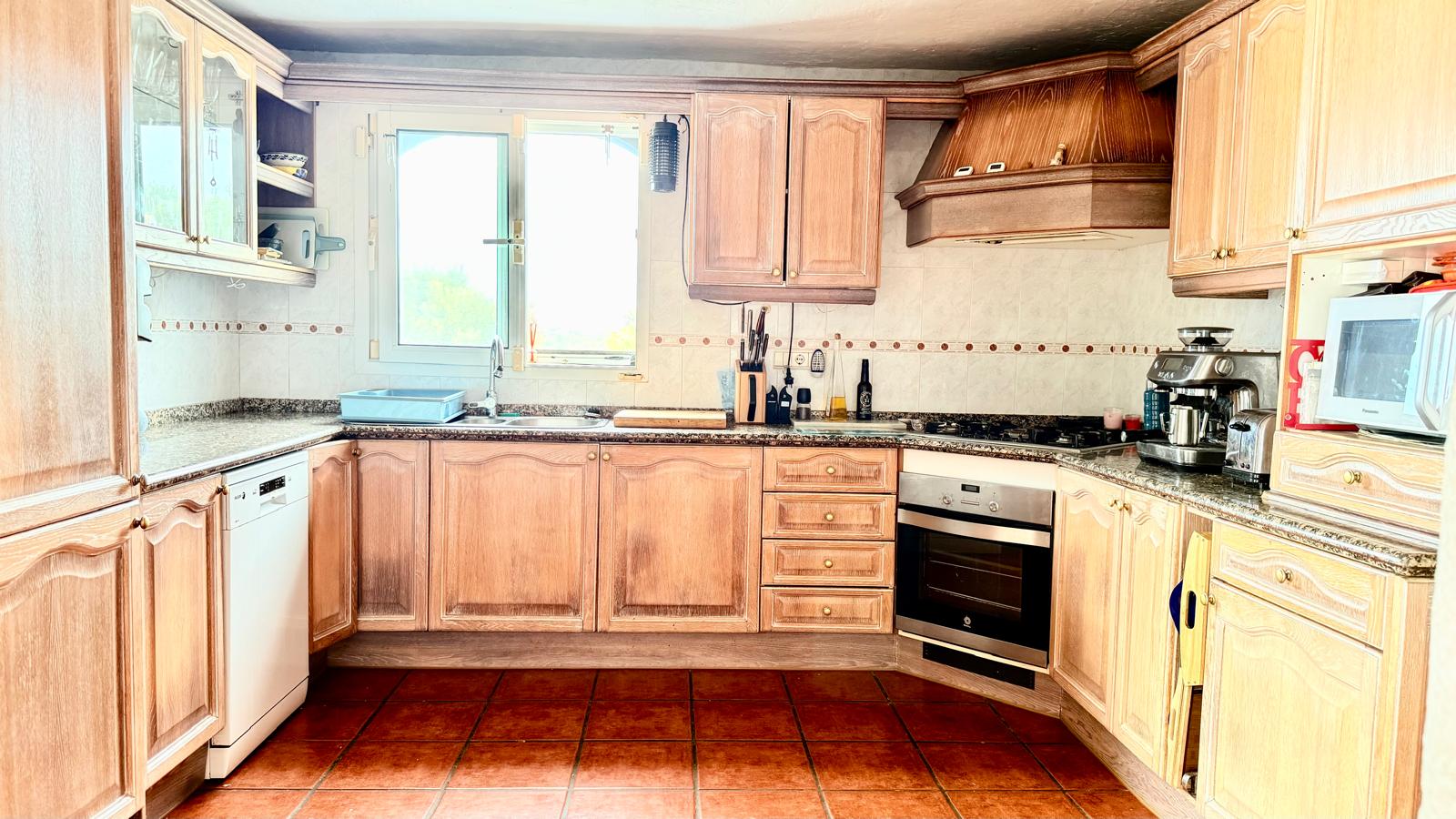 Traditional kitchen featuring oak cabinetry, granite countertops, and terracotta flooring. It includes integrated appliances and a prominent wood-paneled extractor hood.