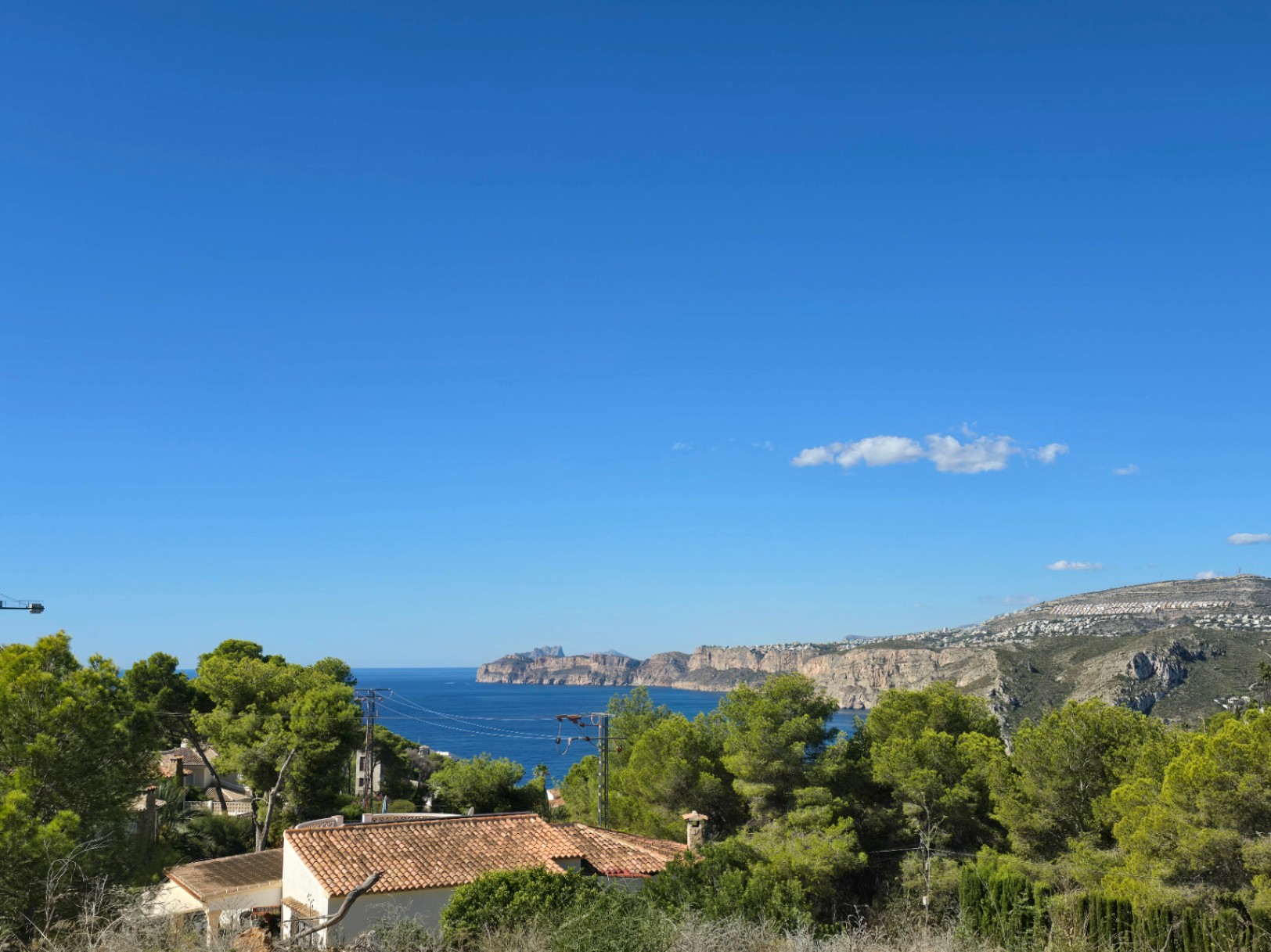 Panoramic views of the Mediterranean Sea and the Javea cliffs from the elevated plot, surrounded by pine trees and native vegetation.