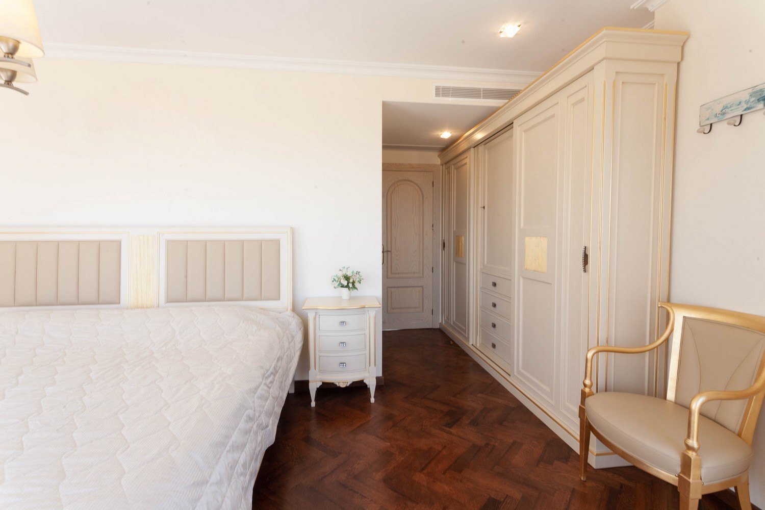 Bedroom featuring a bed with upholstered headboard, light wood built-in wardrobe, and dark parquet flooring.