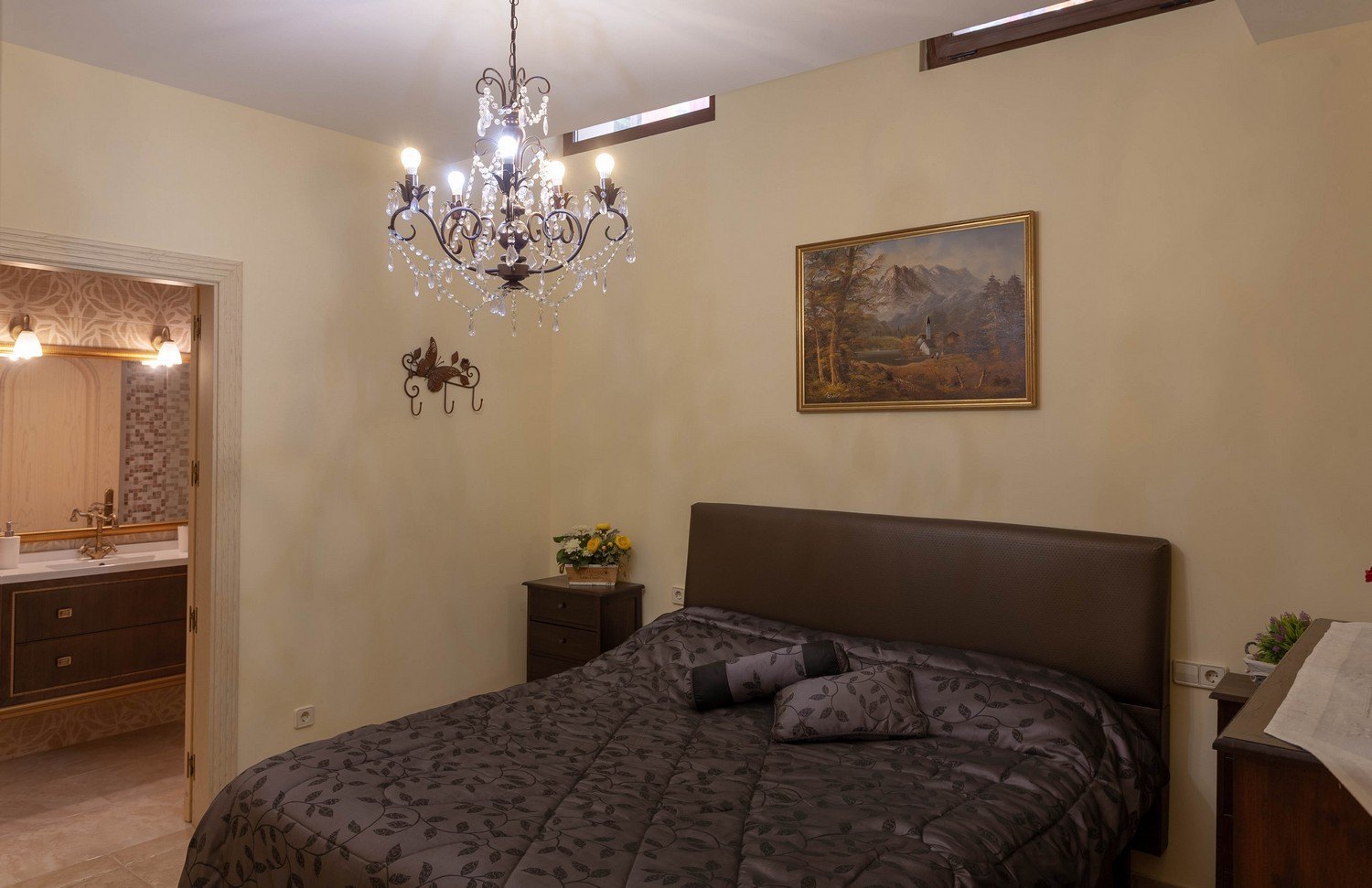 Bedroom featuring a double bed, crystal chandelier, and access to an en-suite bathroom with a double sink.