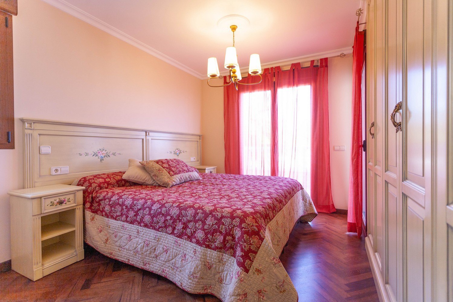 Bedroom featuring a double bed, nightstand, and light wood wardrobe with floral details.