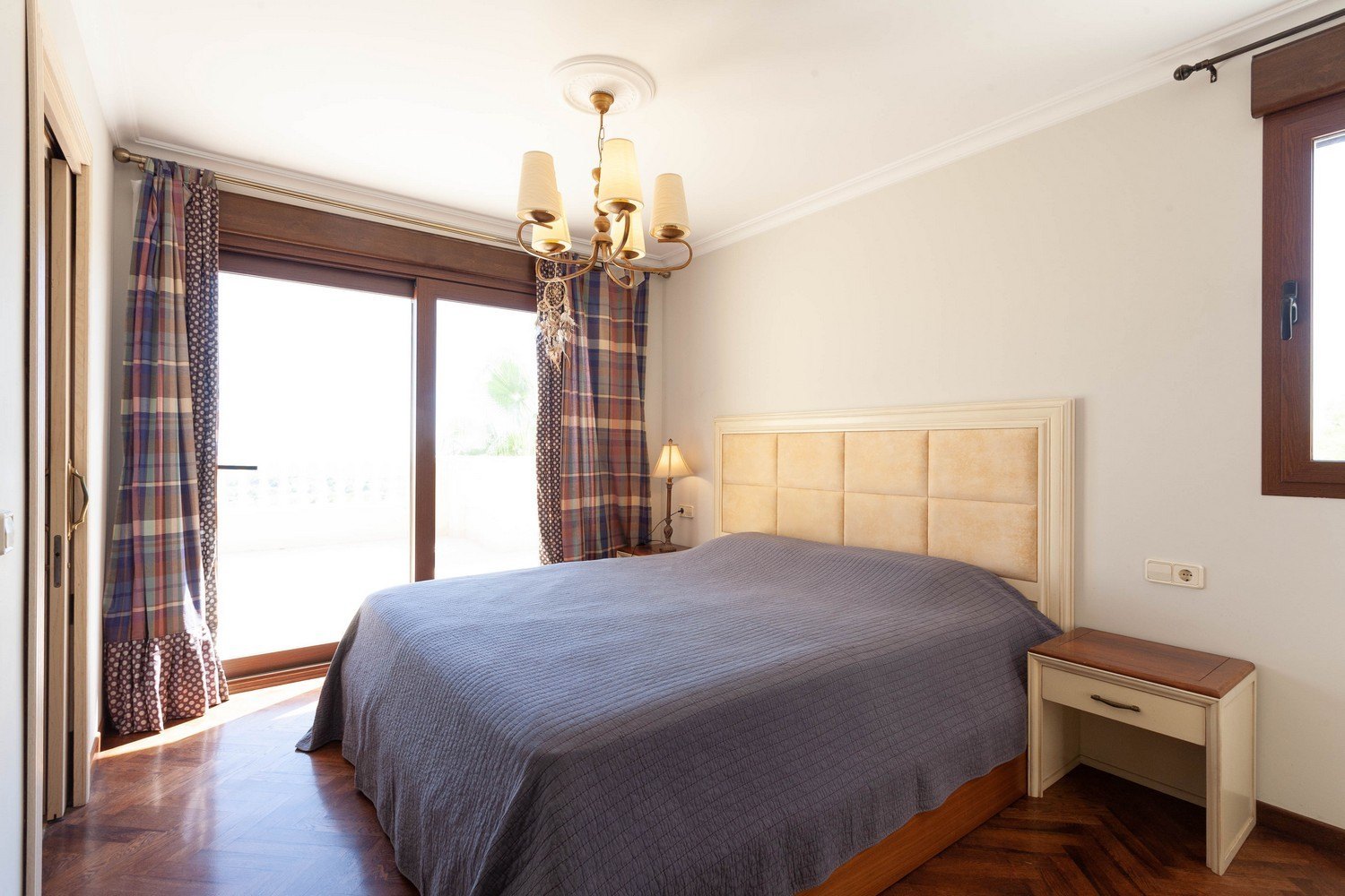 Bedroom with double bed, upholstered headboard, and terrace access. Classic chandelier and patterned curtains.