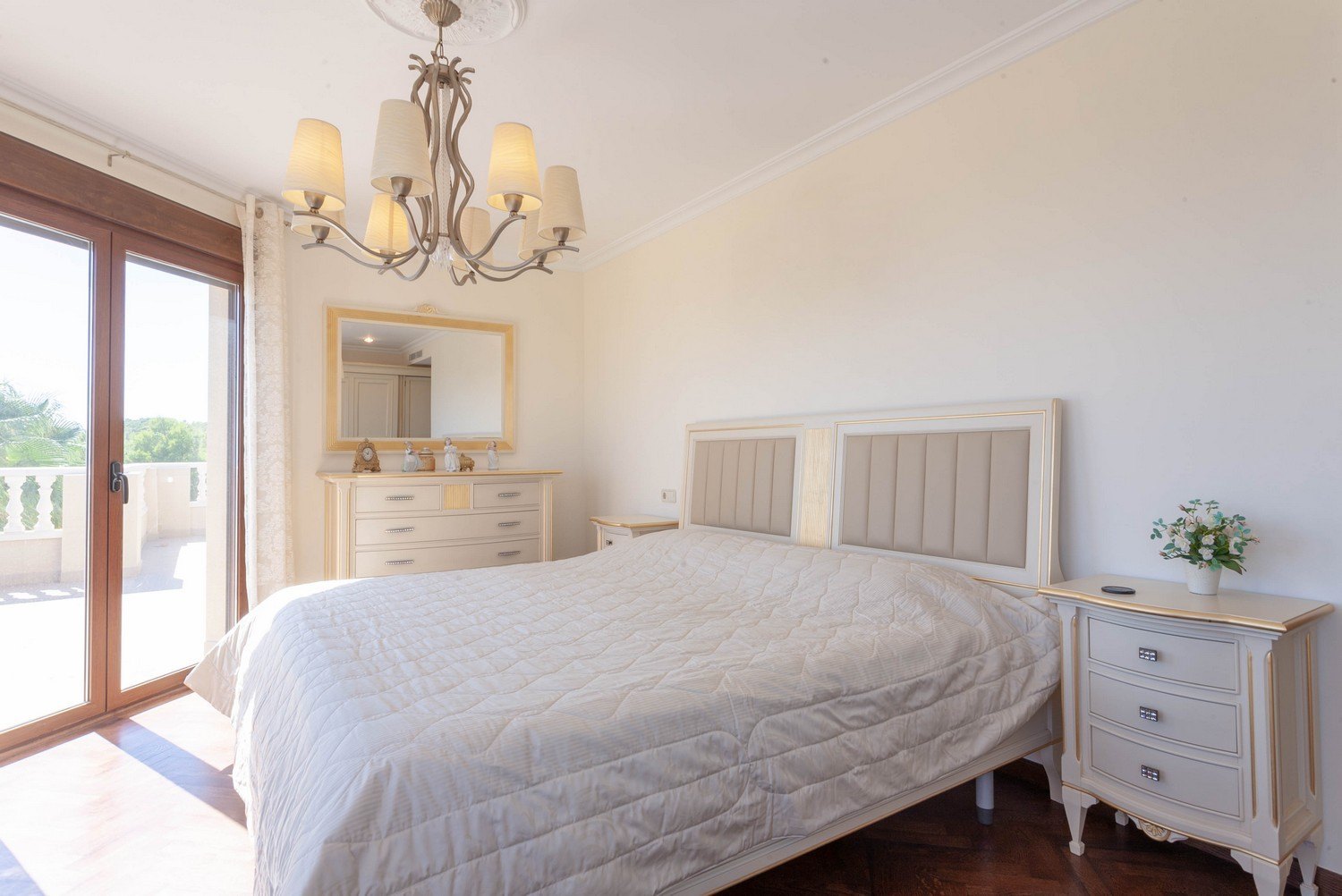 Bright bedroom featuring a double bed, bedside tables, and a classic dresser with a gold-framed mirror.