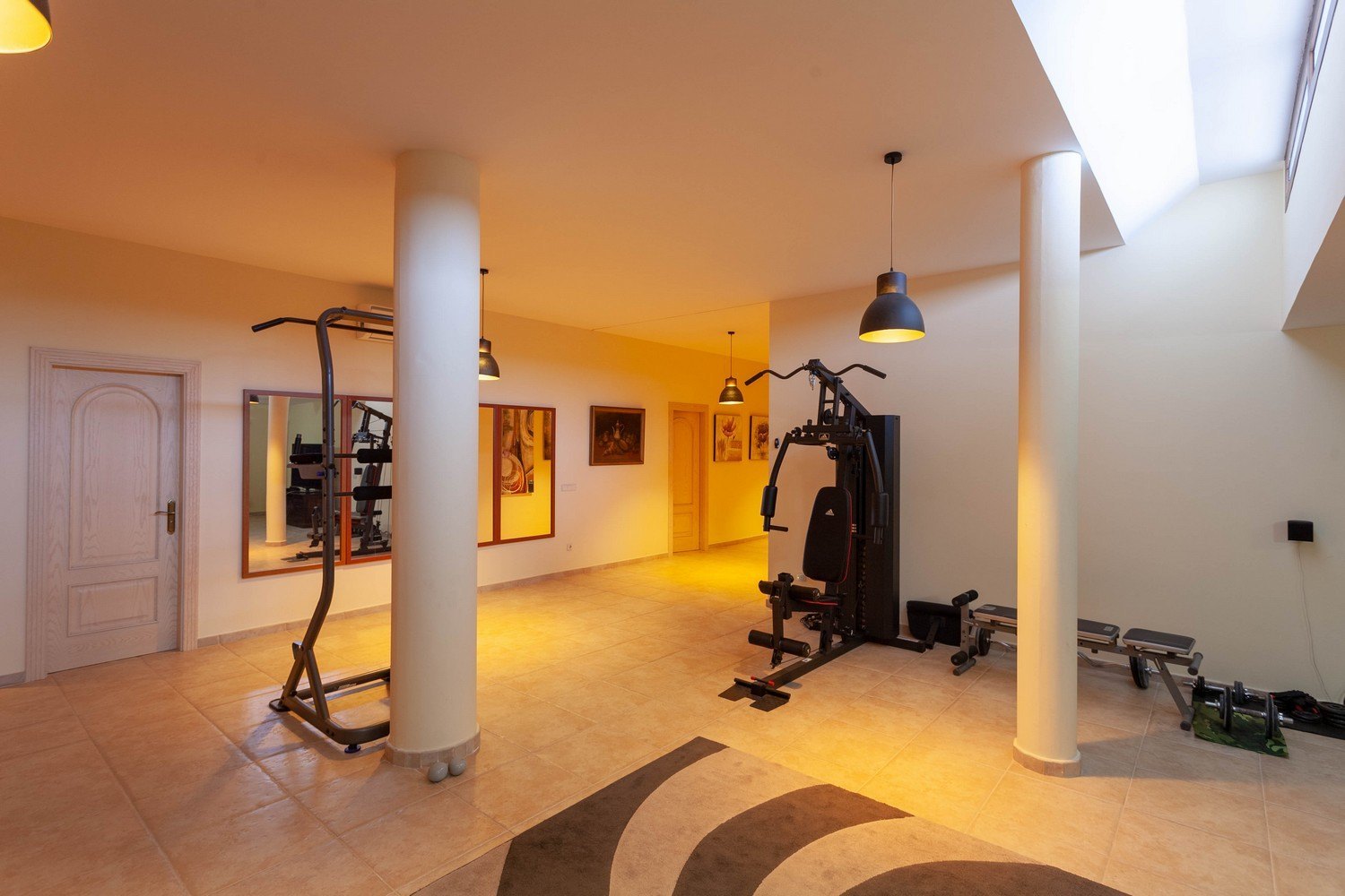 Bright gym with tile flooring, equipped with exercise machines and overhead natural light.