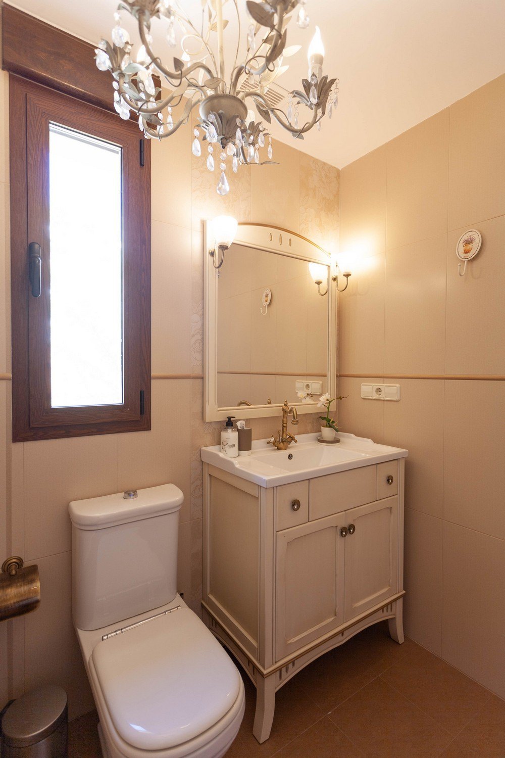 Classic bathroom detail with wood vanity and white countertop, mirror with sconces, and crystal chandelier.