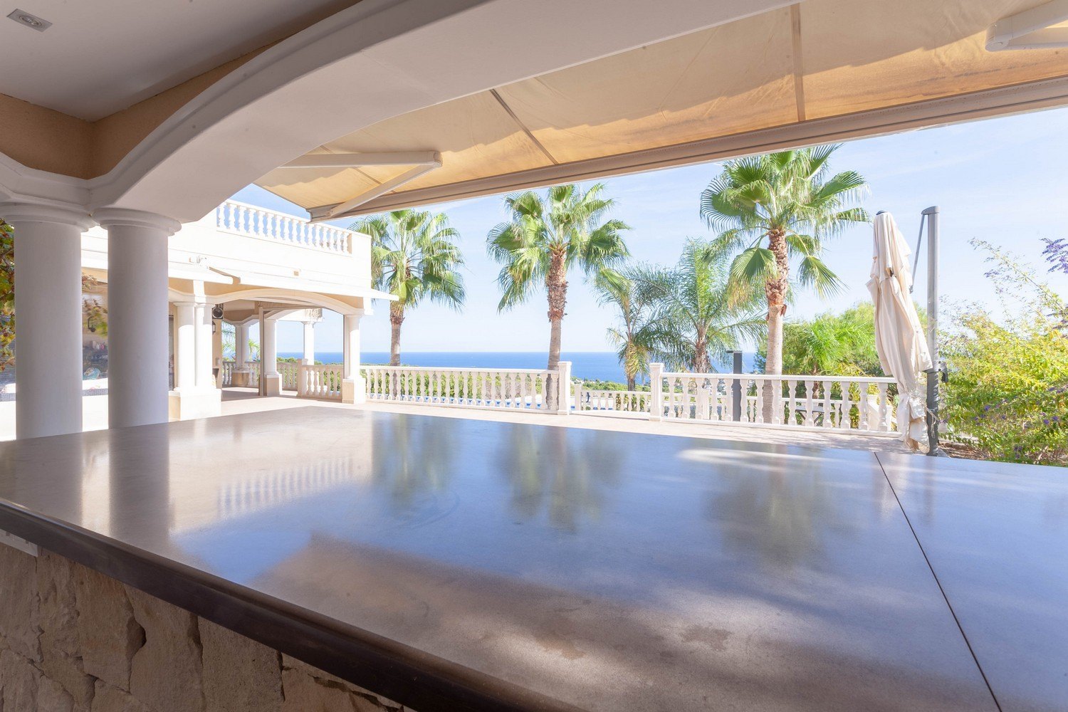 Covered terrace featuring a stone bar, overlooking the sea and palm trees in Raco de Galeno, Benissa.