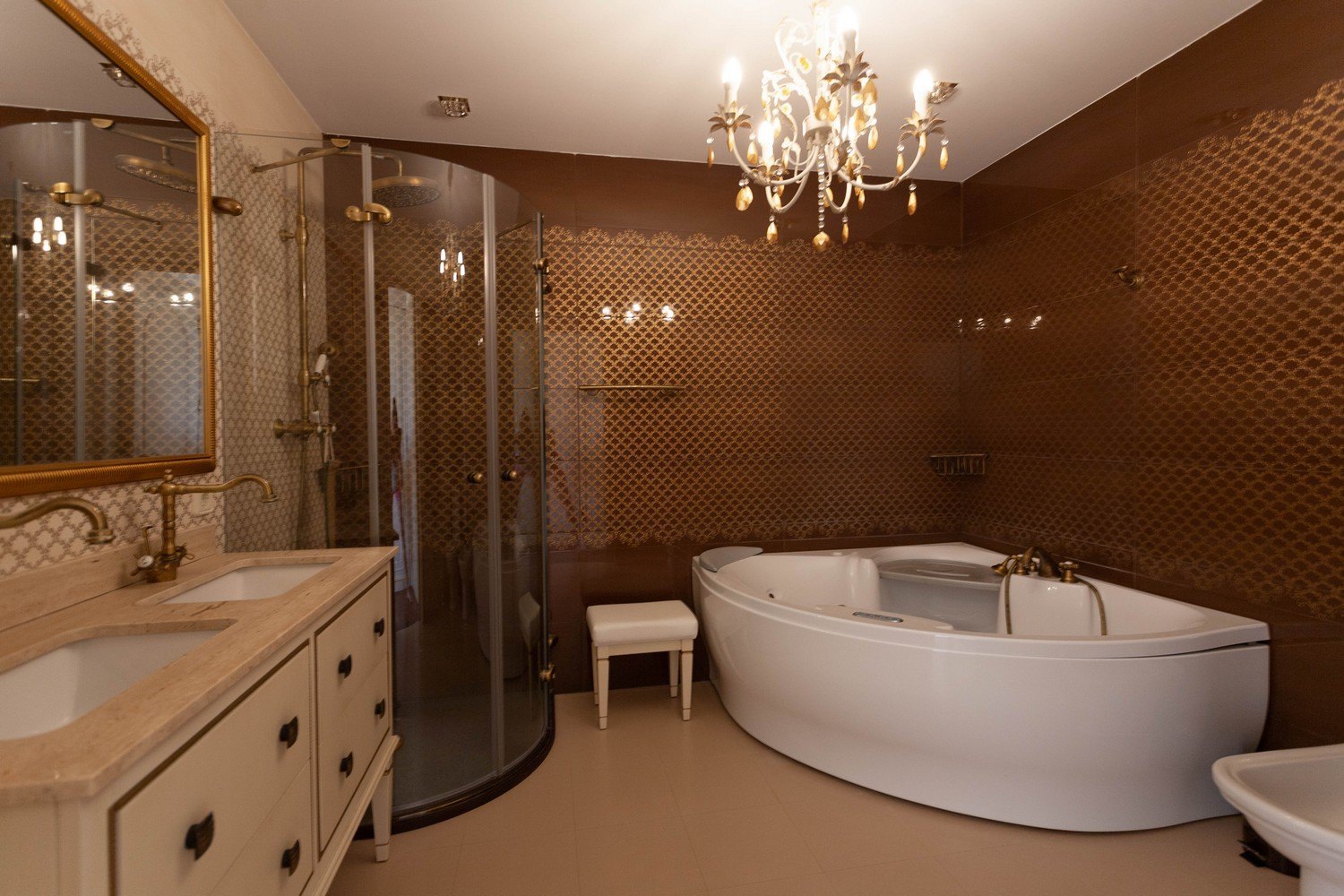 Elegant bathroom featuring a jetted tub, curved glass shower, and double vanity with gold fixtures.