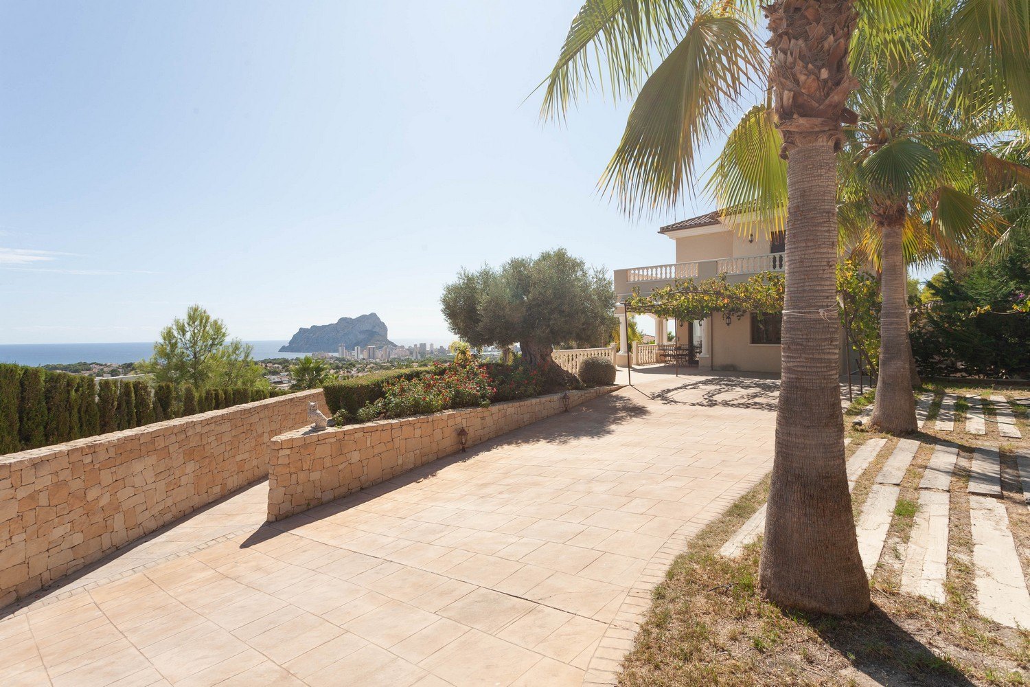 Exterior view of the villa with tiled pathway, stone wall, and sea views.