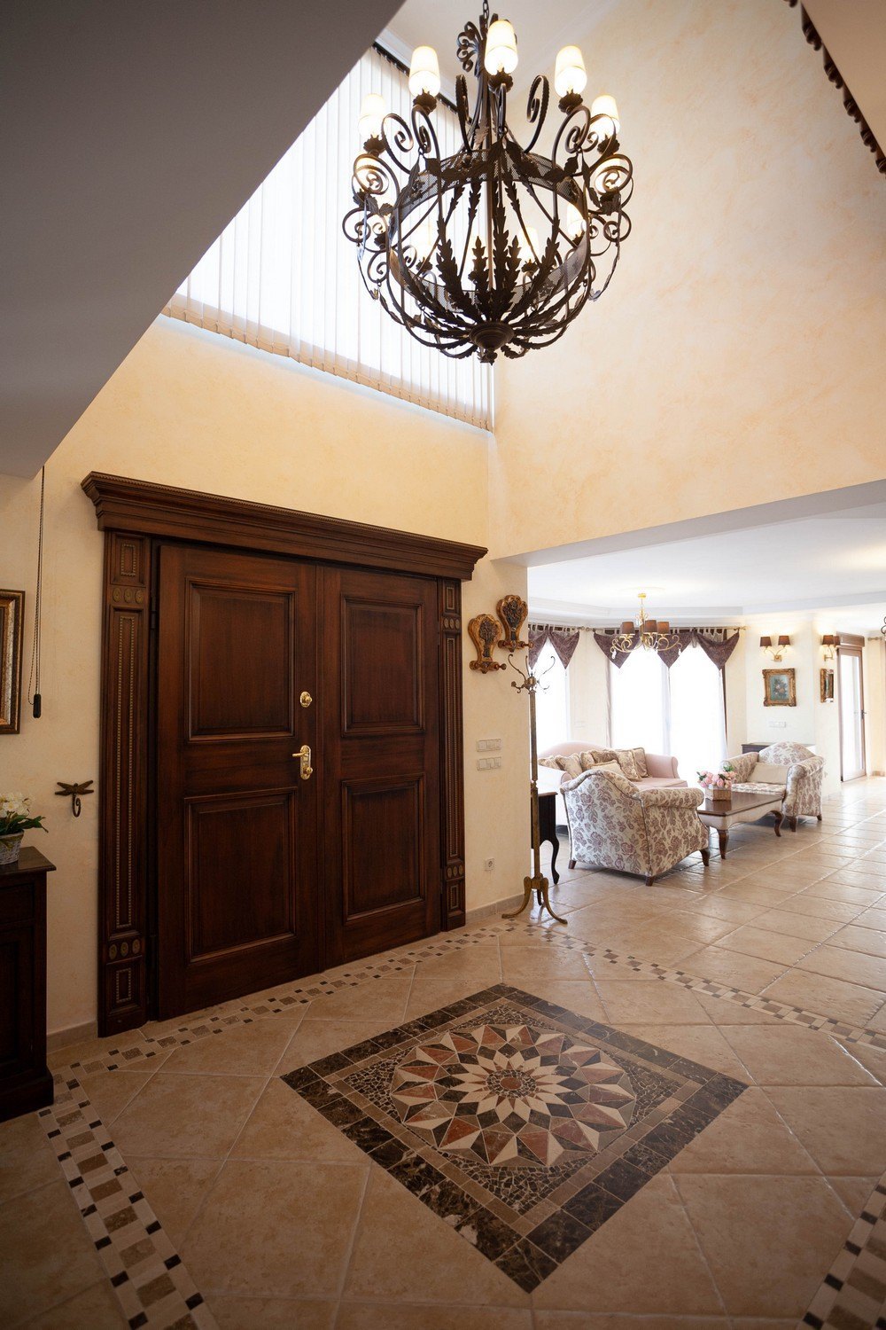 Foyer featuring dark wood double doors and ornate chandelier. Tiled flooring with geometric design.