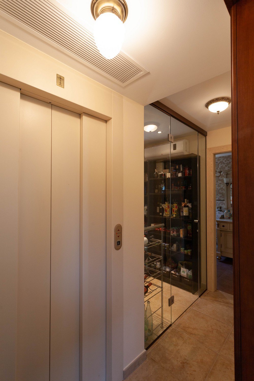 Interior elevator detail next to a glass-enclosed pantry with metal shelving.
