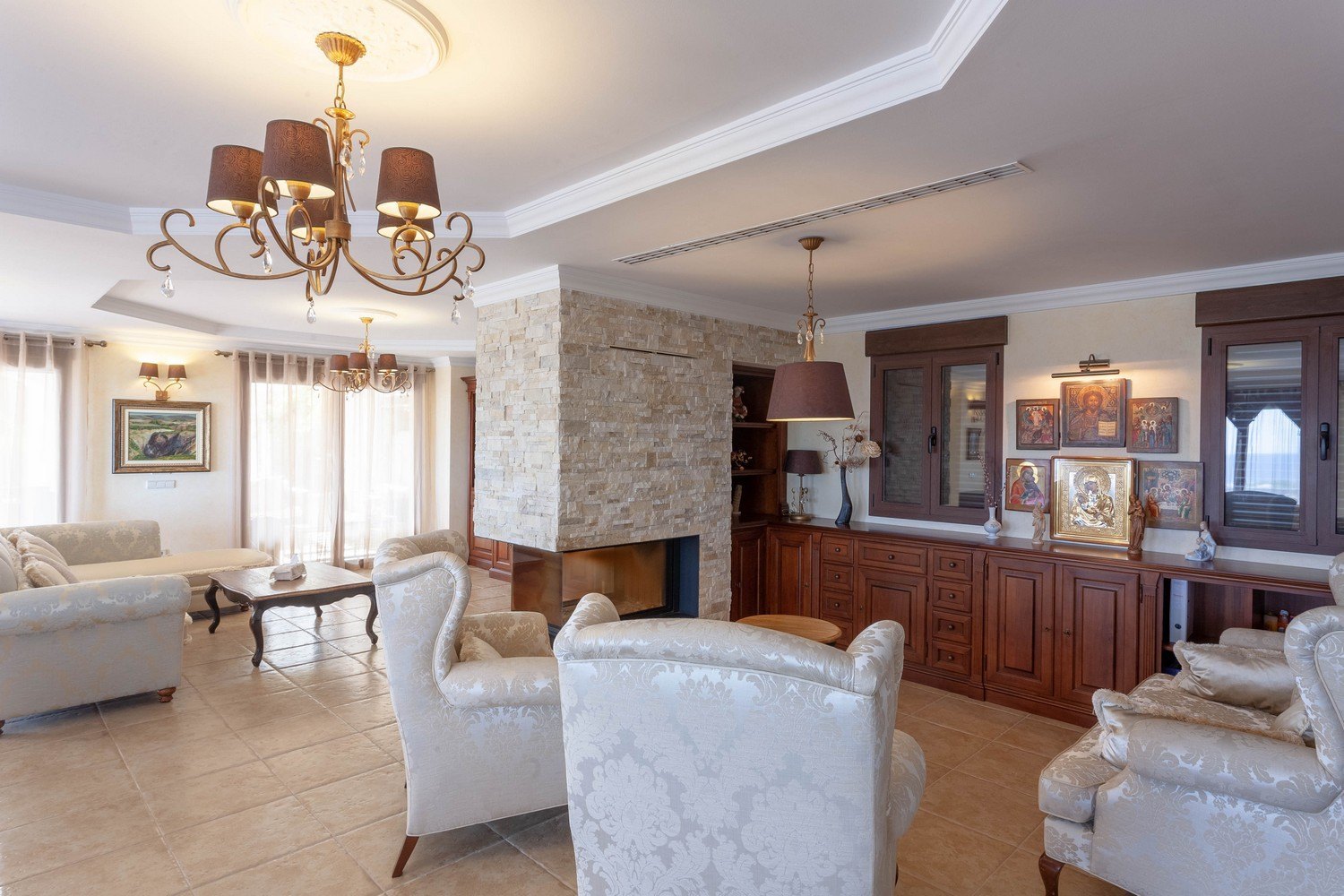 Living room with stone-clad fireplace, classic wood furniture, and ceramic tile flooring.