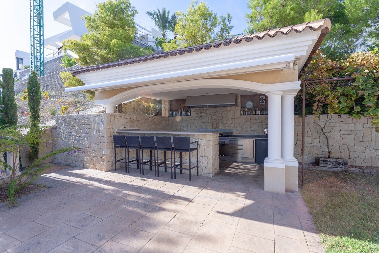 Outdoor barbecue area with bar and stools in Benissa villa. Stone cladding and stainless steel countertop.