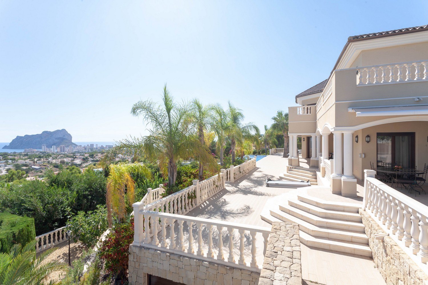 Terrace view with stone balustrade, palm trees, and views of the sea and Peñón de Ifach.