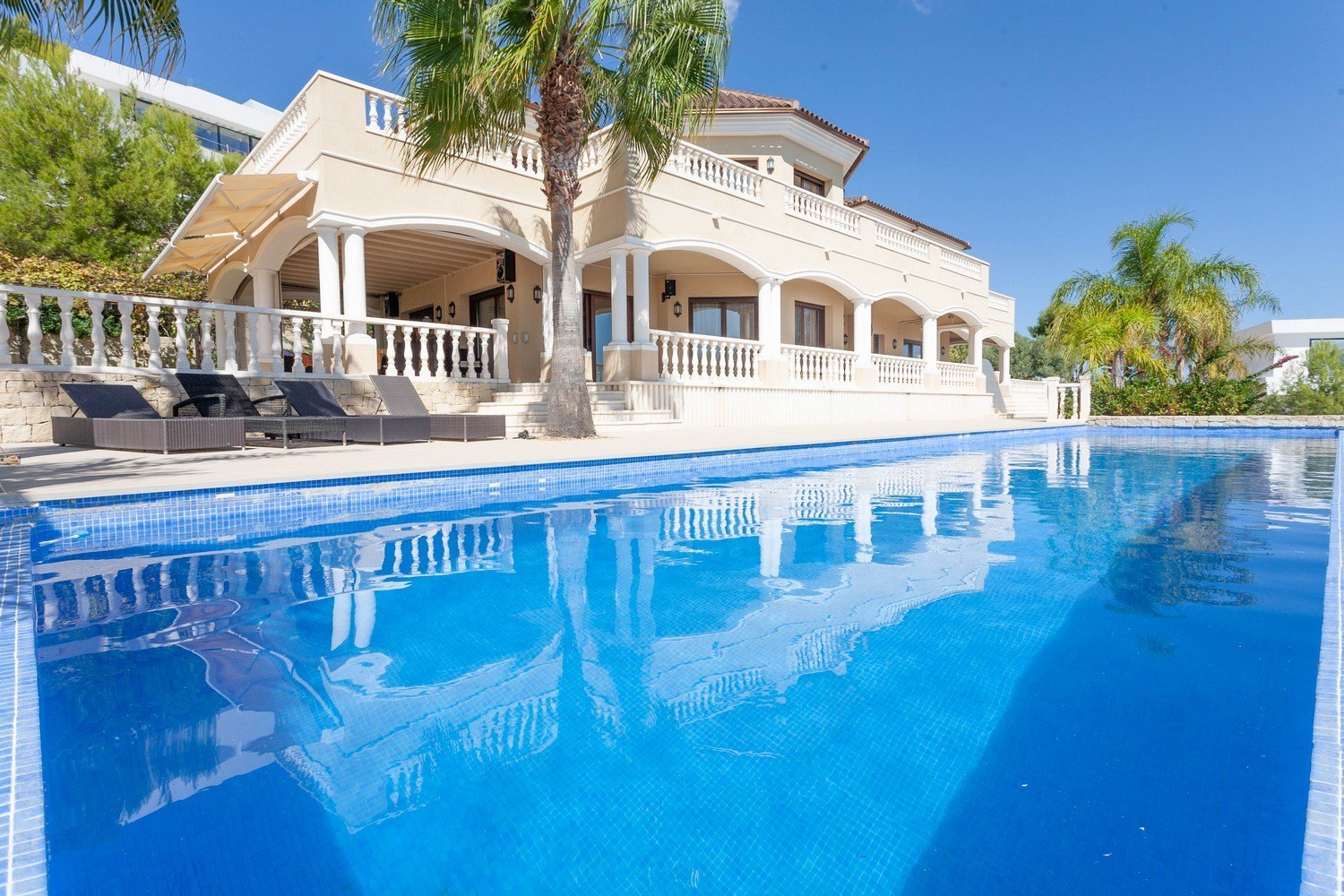 View of the blue-tiled "Infinity" pool and the facade of the Mediterranean villa with columns.