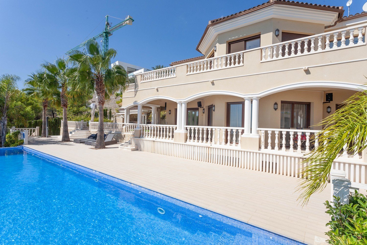 View of the pool and facade of the Mediterranean villa with white baluster railing.