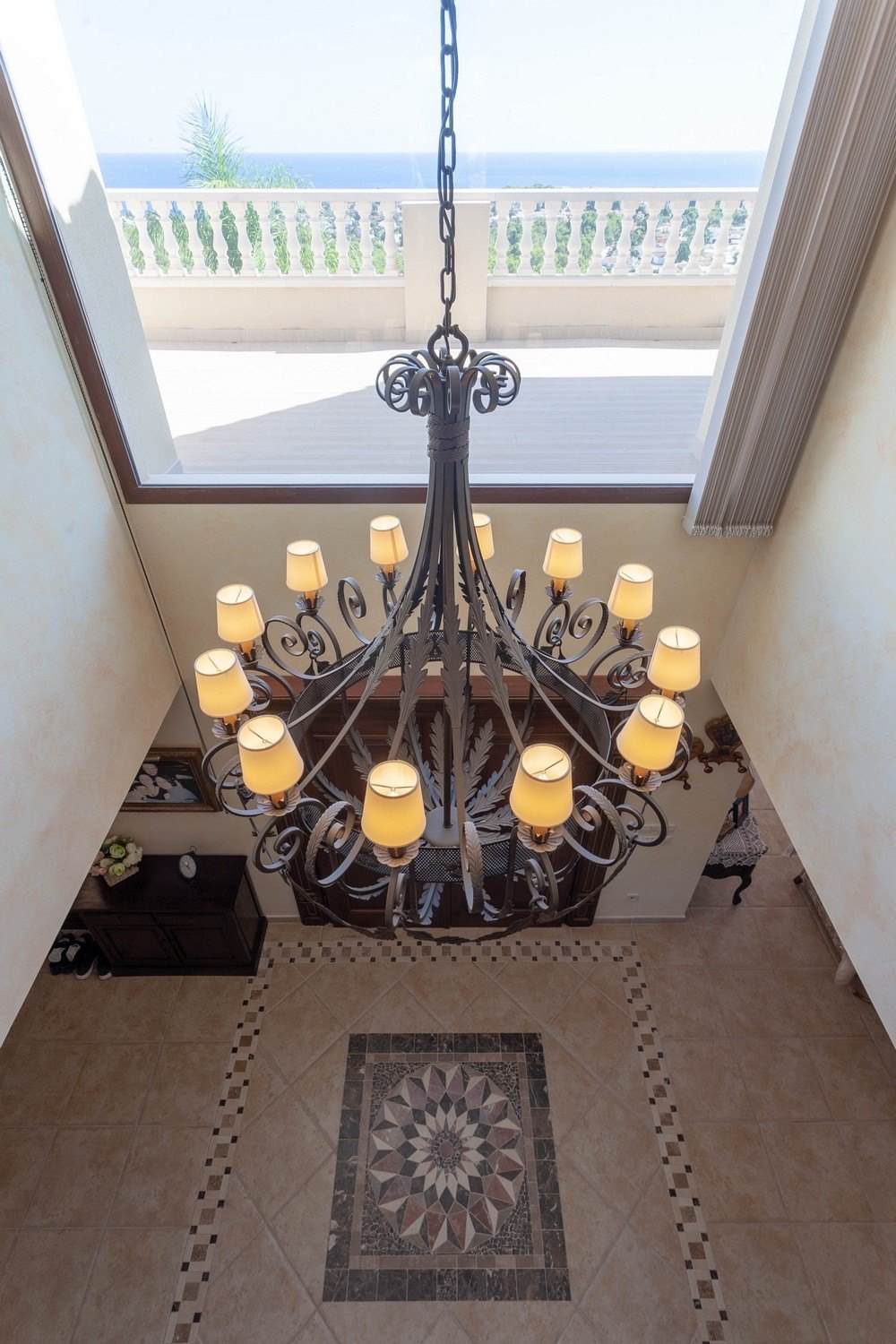 Wrought iron chandelier detail over decorated ceramic floor and sea views.