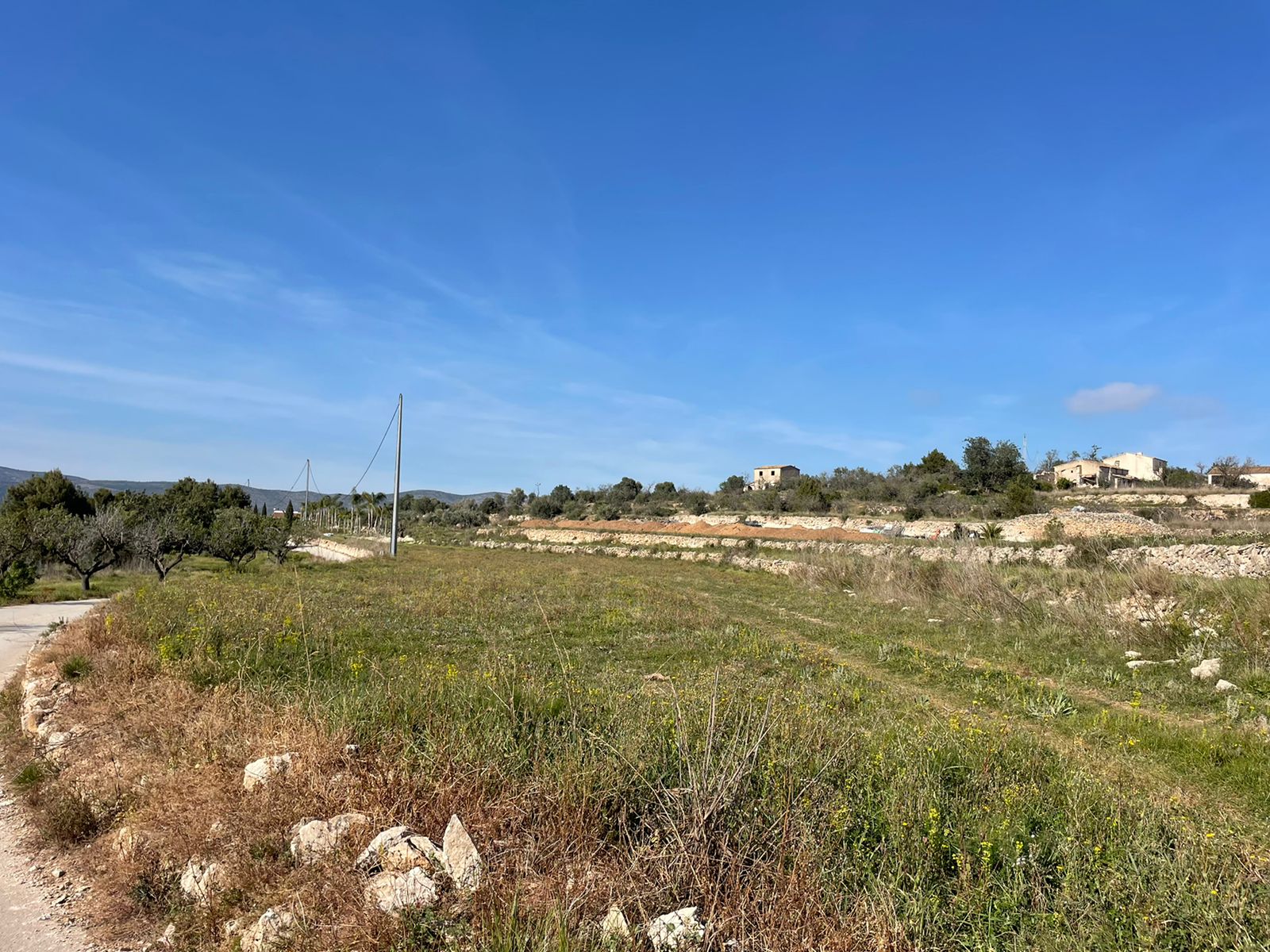 View of rustic land in Jávea with elevated constructions and a clear blue sky.