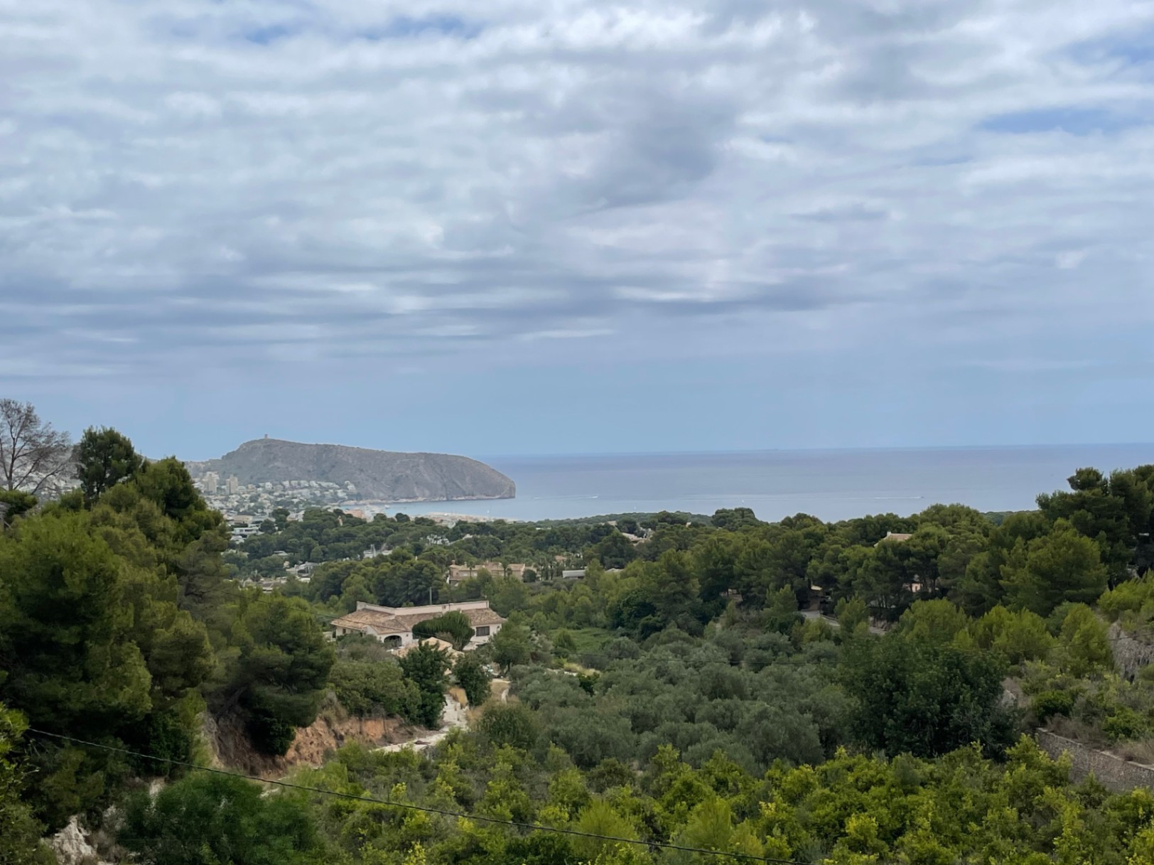 Panoramic view from the Benimeit plot, overlooking a lush Mediterranean valley toward the sea and the distinctive Cap d'Or headland in Moraira.