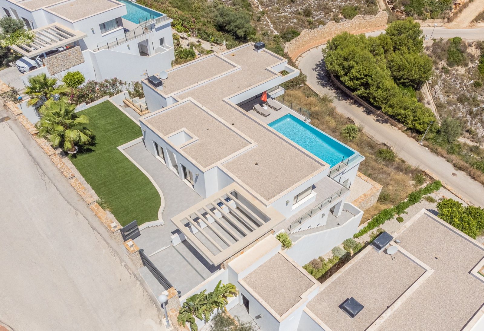 Aerial perspective of the modern villa featuring a tiered white facade, infinity pool, flat gravel roofs, and a manicured artificial lawn.