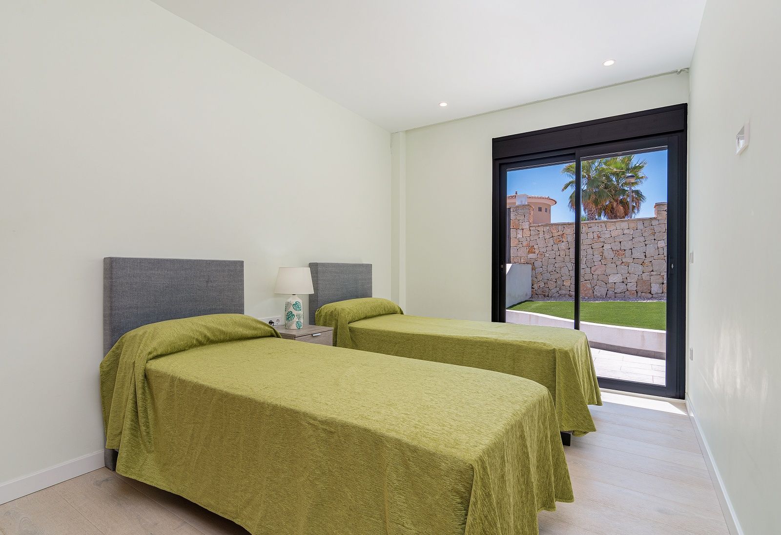Bedroom featuring twin beds with grey headboards and sliding glass doors opening onto a private terrace with a natural stone wall.