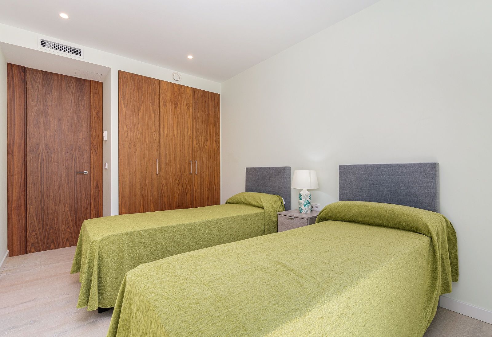 Bright bedroom featuring twin beds with grey headboards, integrated wooden wardrobes, and ducted air conditioning for climate control.