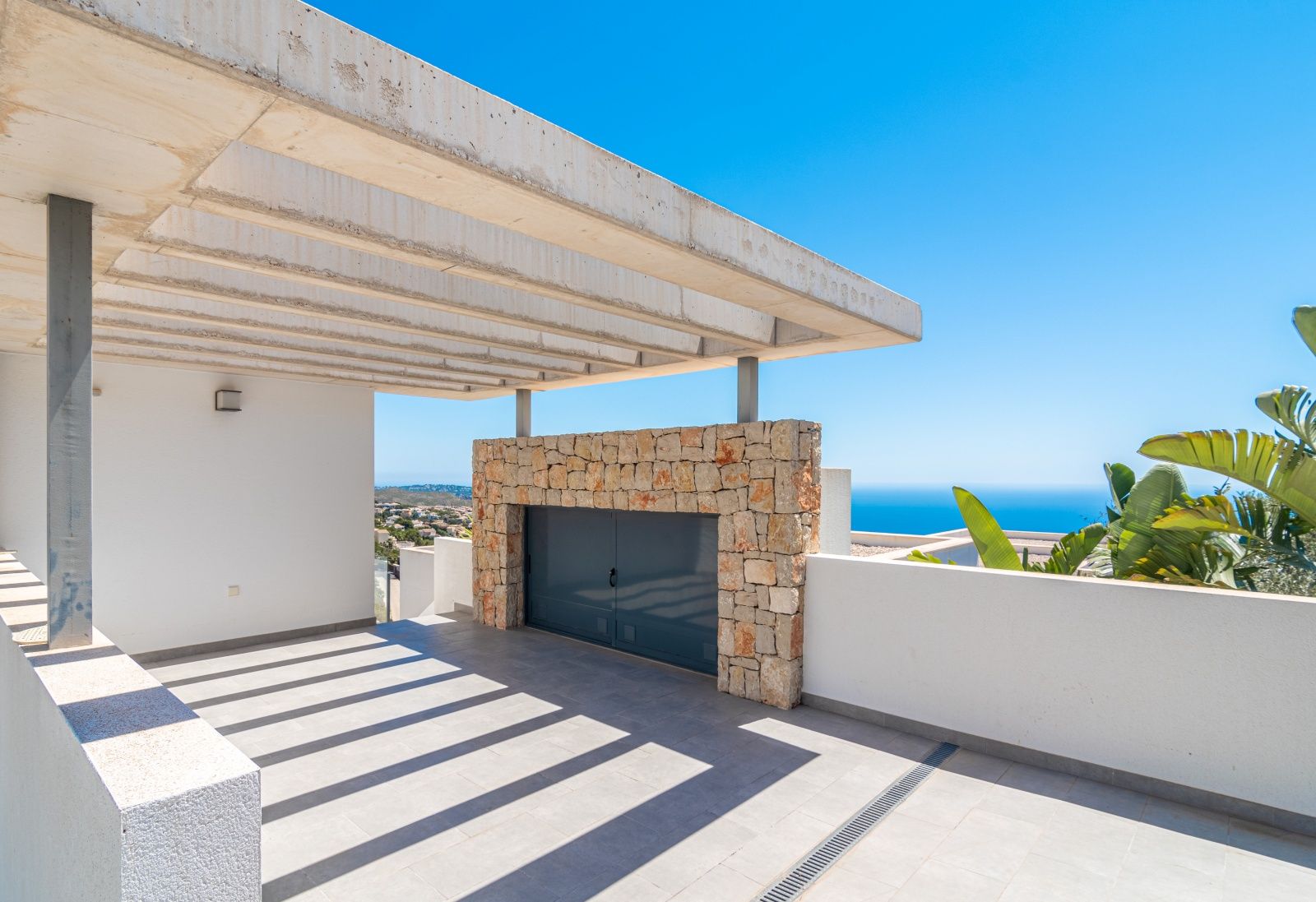 Covered parking area featuring an exposed concrete pergola, natural stone wall accents, and expansive views of the Mediterranean Sea.