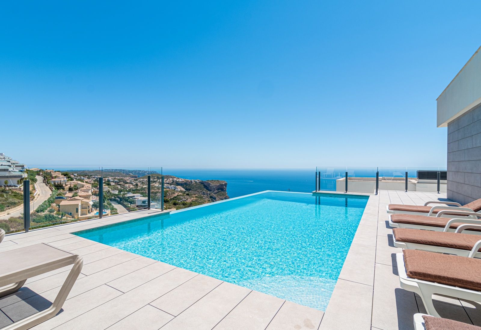 Infinity pool overlooking the Mediterranean Sea, featuring a large tiled terrace with sun loungers and modern glass safety railings.