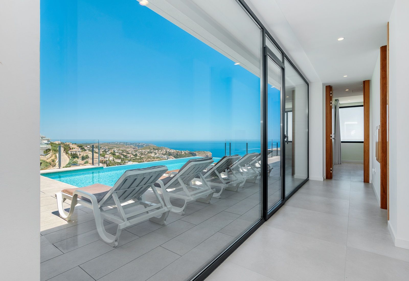 Interior hallway featuring floor-to-ceiling glass doors that open to a sun terrace with an infinity pool and expansive Mediterranean views.