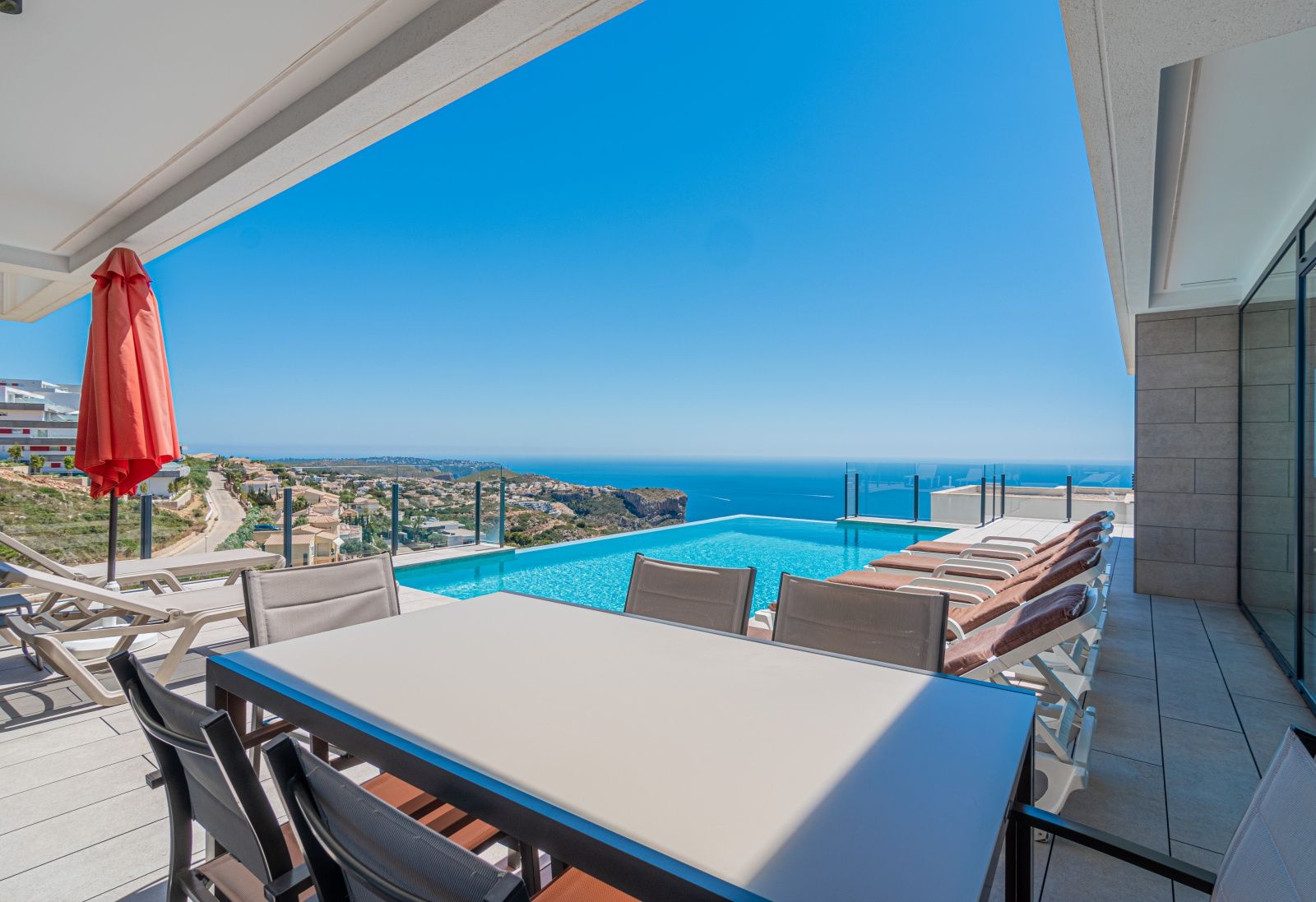 Main terrace featuring an infinity pool, outdoor dining area, and panoramic views of the Mediterranean Sea and Benitachell coastline.
