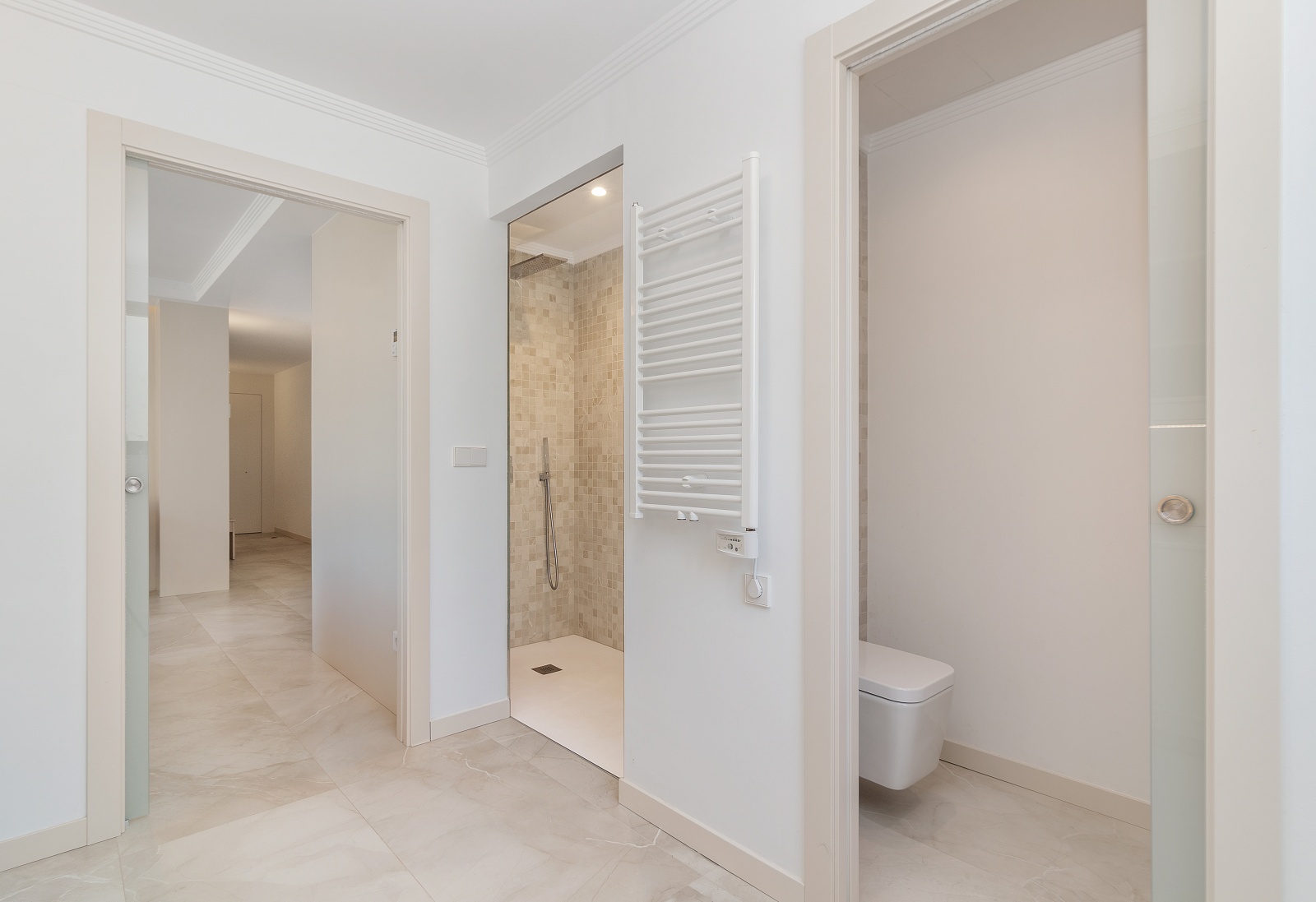 Modern bathroom featuring a walk-in mosaic shower, wall-mounted toilet, white heated towel rail, and glass sliding doors with marble-effect flooring.