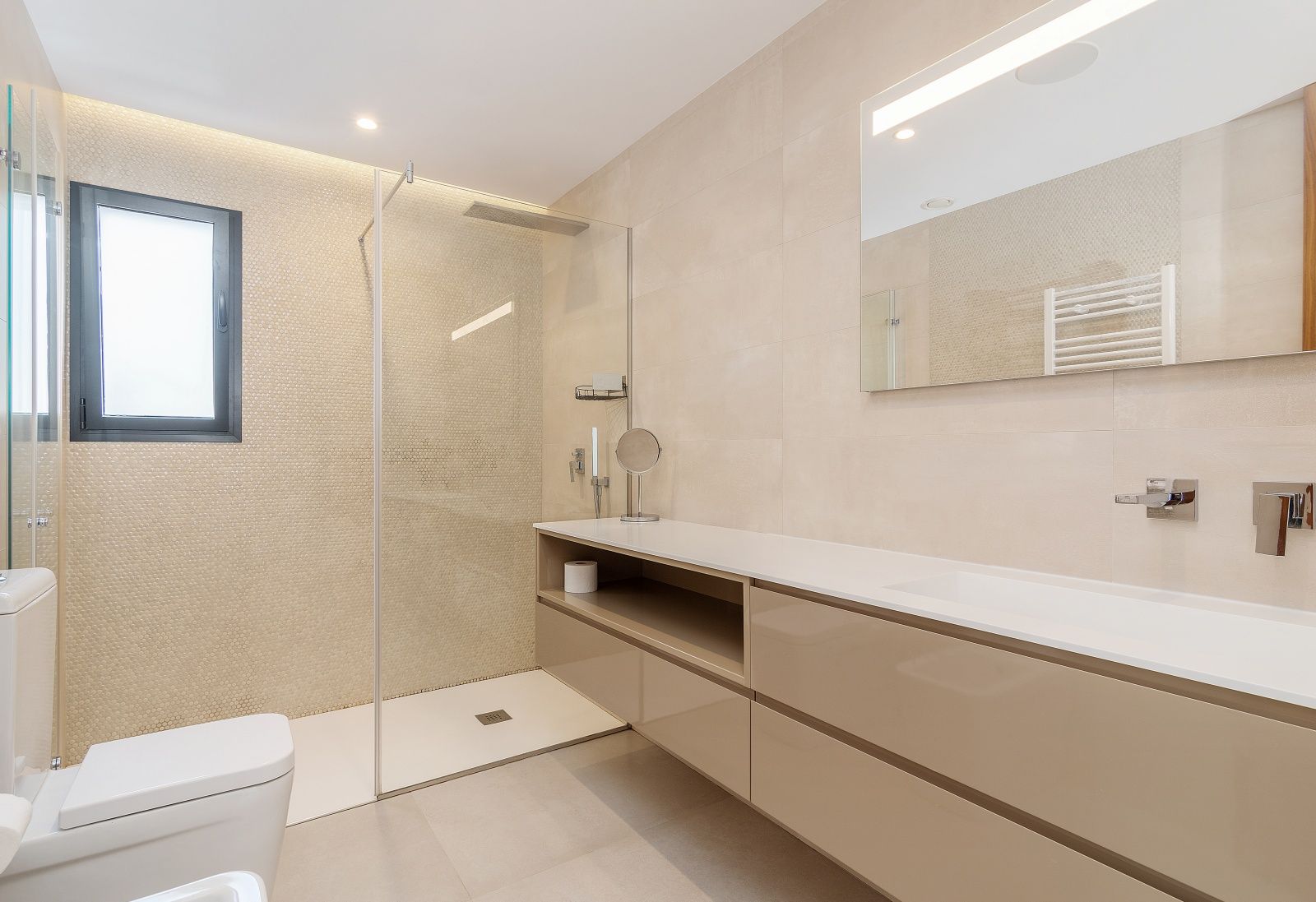Modern bathroom featuring a walk-in shower with glass partition and mosaic tiling. Equipped with a floating beige vanity, integrated sink, and LED-backlit mirror.