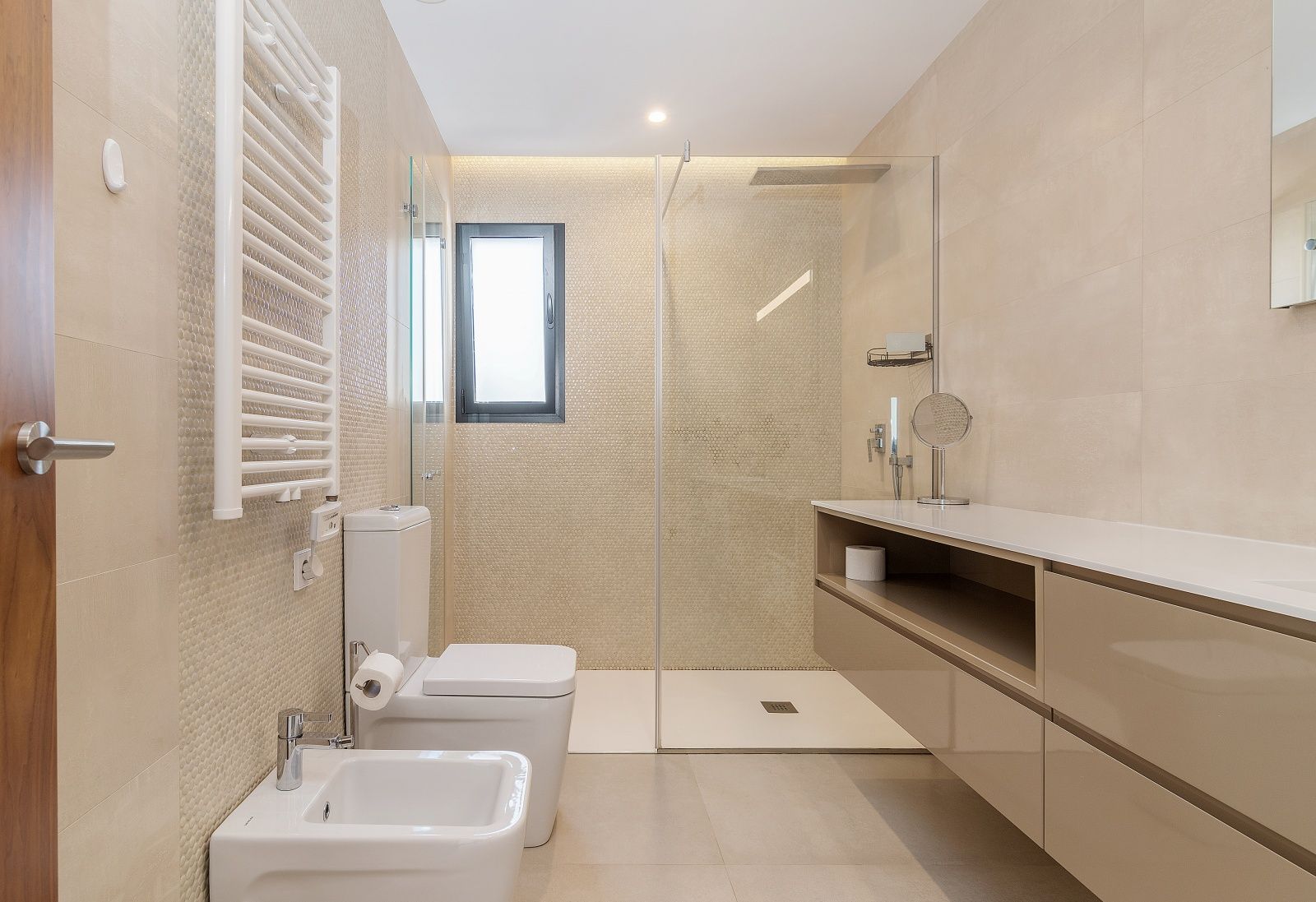 Modern bathroom featuring a walk-in shower with glass partition, mosaic tiling, wall-mounted vanity, bidet, and a white heated towel rail.