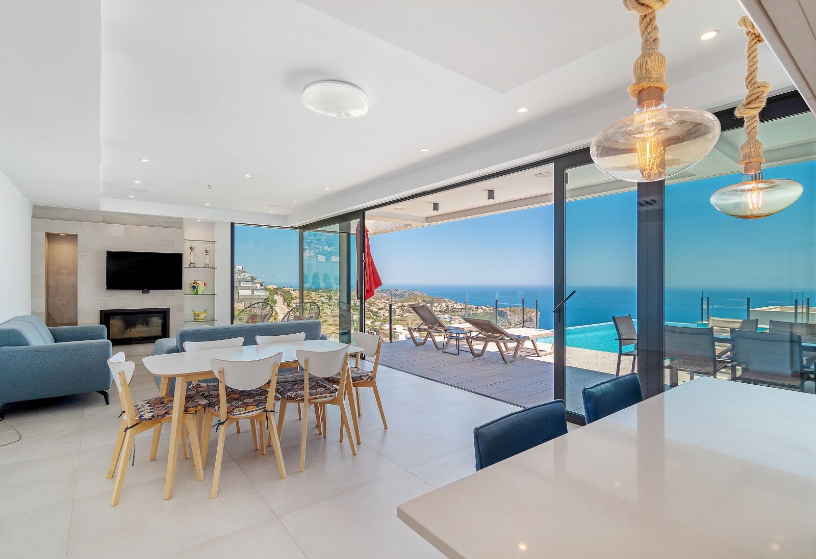 Open-plan living and dining area featuring floor-to-ceiling glass doors that open to a terrace with an infinity pool and expansive sea views.