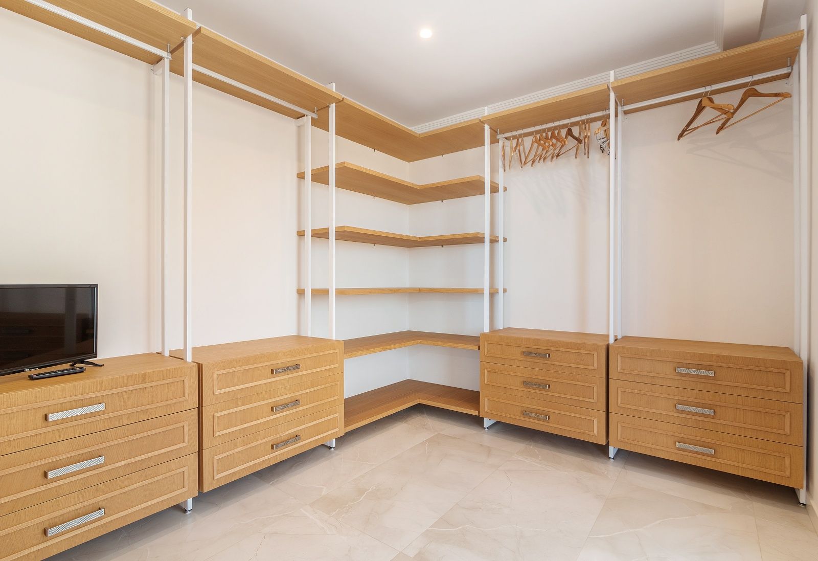 Open walk-in closet featuring light wood shelving, integrated drawer units, and marble-effect porcelain flooring with recessed ceiling lighting.