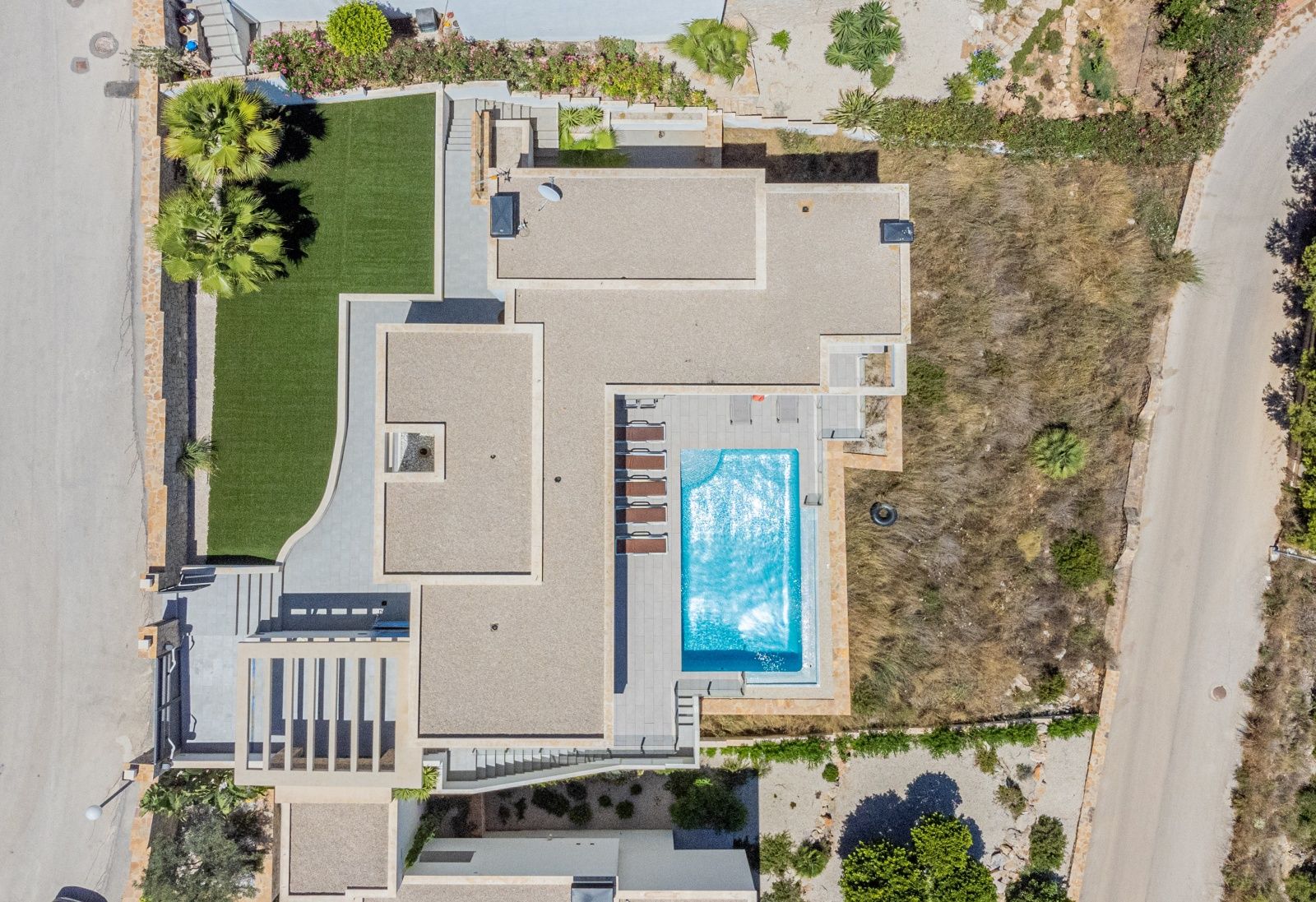 Zenithal aerial view of the villa showcasing the plot layout, the rectangular swimming pool with sun terrace, flat gravel roofs, and landscaped garden areas.
