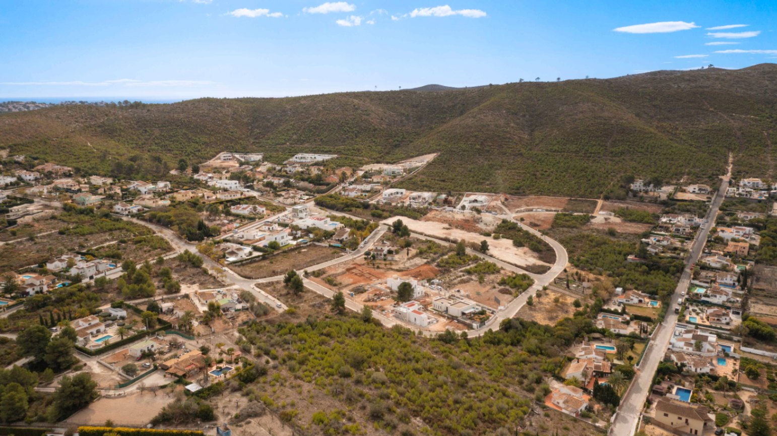 Aerial panorama of the Lomas Del Rey urbanization in Jávea, showcasing the layout of residential plots among Mediterranean hills and pine forests.
