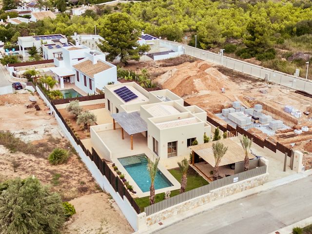 Aerial view of the modern villa featuring rooftop solar panels, a private swimming pool, and landscaped gardens with Mediterranean palm trees.