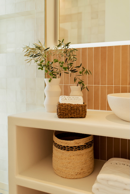 Bathroom detail featuring a built-in vanity with open shelving, vertical terracotta tiles, and a vessel sink. Natural textures and olive branch decor enhance the Mediterranean feel.