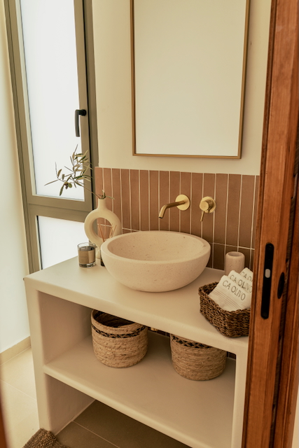 Modern bathroom featuring a stone vessel sink, brushed gold wall-mounted fixtures, and a vertical terracotta tile backsplash.