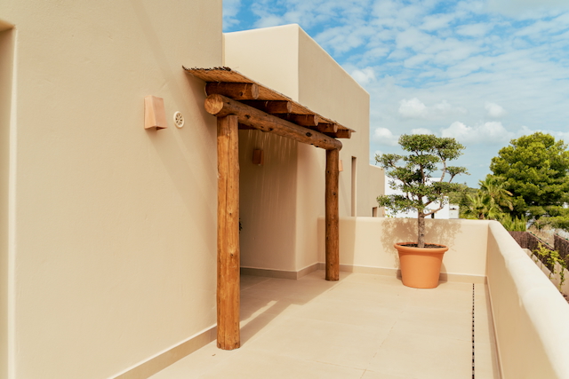Upper terrace featuring a rustic wooden log pergola with a reed roof, a large terracotta planter with an ornamental tree, and clean-lined beige architecture.