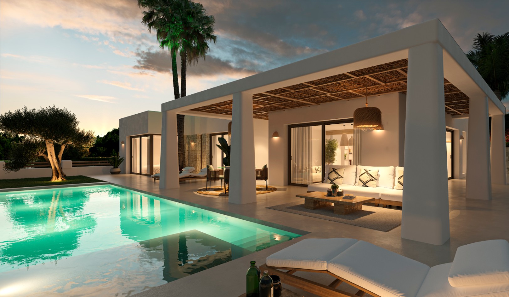 Ibizan-style covered terrace featuring a reed ceiling, outdoor lounge, and an illuminated swimming pool set against a Mediterranean sunset.