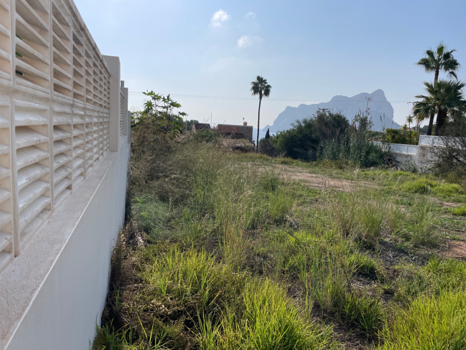 An 856 m² building plot in Bassetes, Calpe, featuring a white perimeter wall and clear, distant views of the iconic Peñón de Ifach rock.