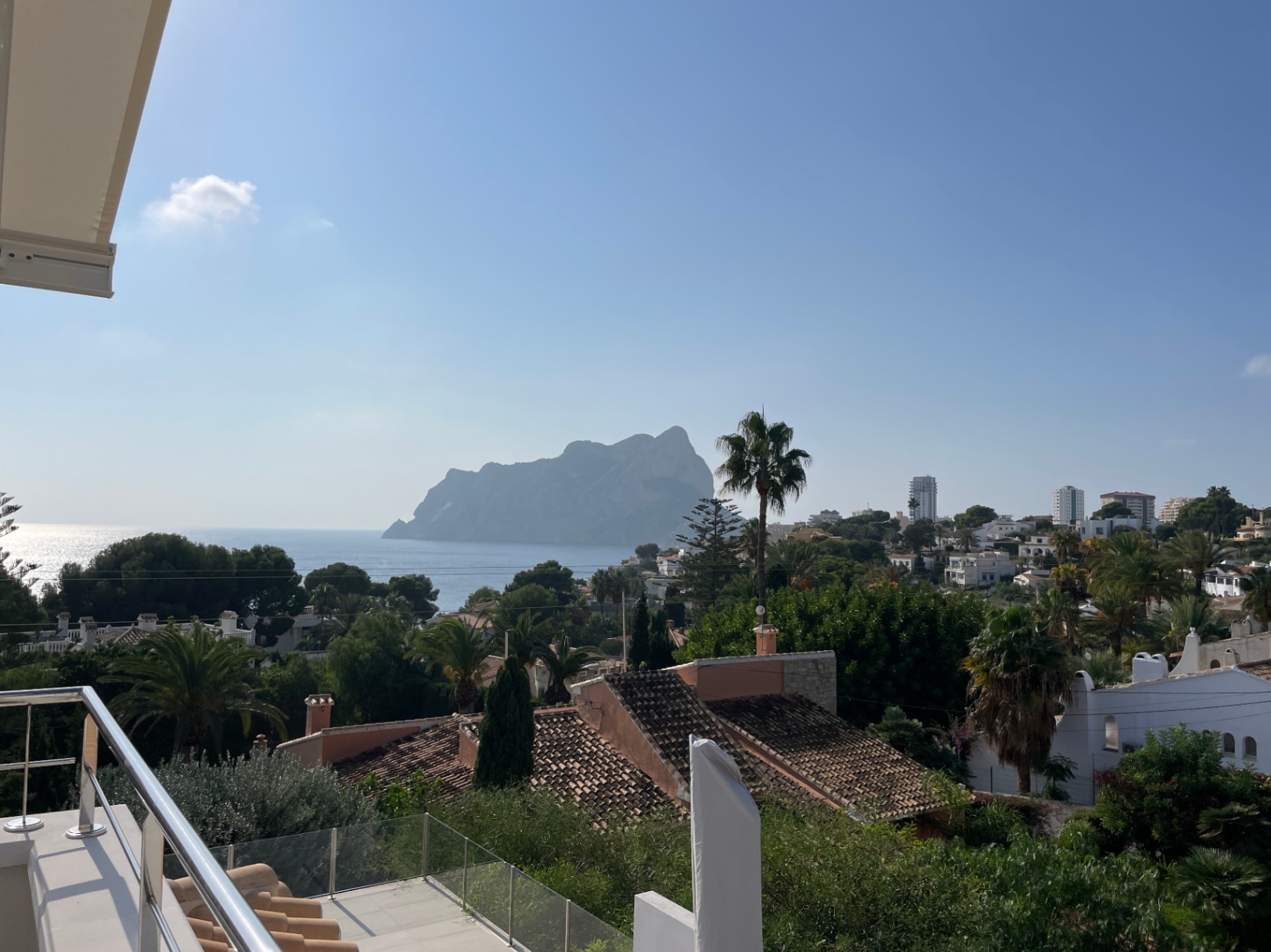 Panoramic view from a terrace with steel and glass railings, overlooking the Peñón de Ifach, the Mediterranean Sea, and local coastal architecture.