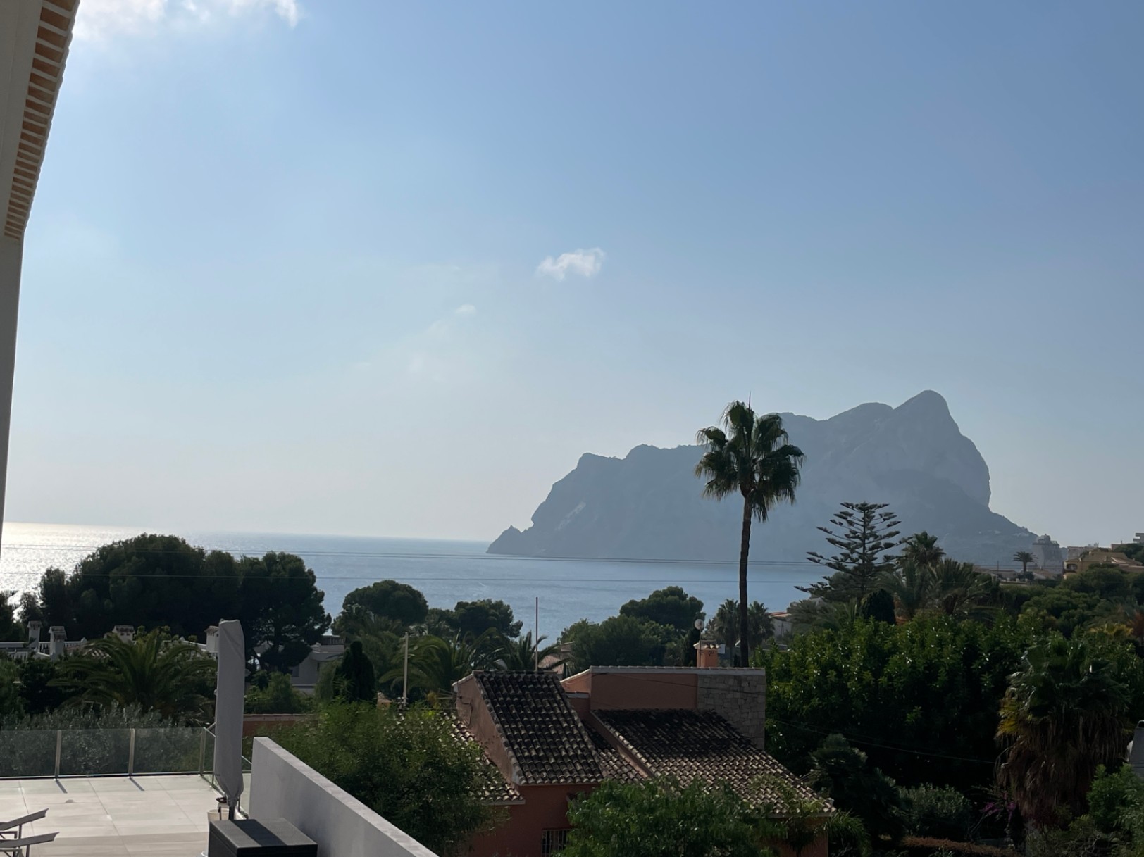 Panoramic views of the Peñón de Ifach and the Mediterranean Sea from an elevated terrace featuring modern glass railings and lush coastal vegetation.
